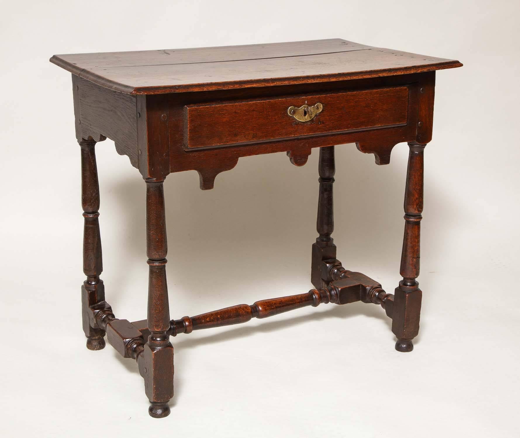 Very fine English oak side table, the richly patinated two plank top with molded edge over single drawer with original lock and etched escutcheon, over double stepped arched apron over richly turned legs joined by turned stretchers and standing on