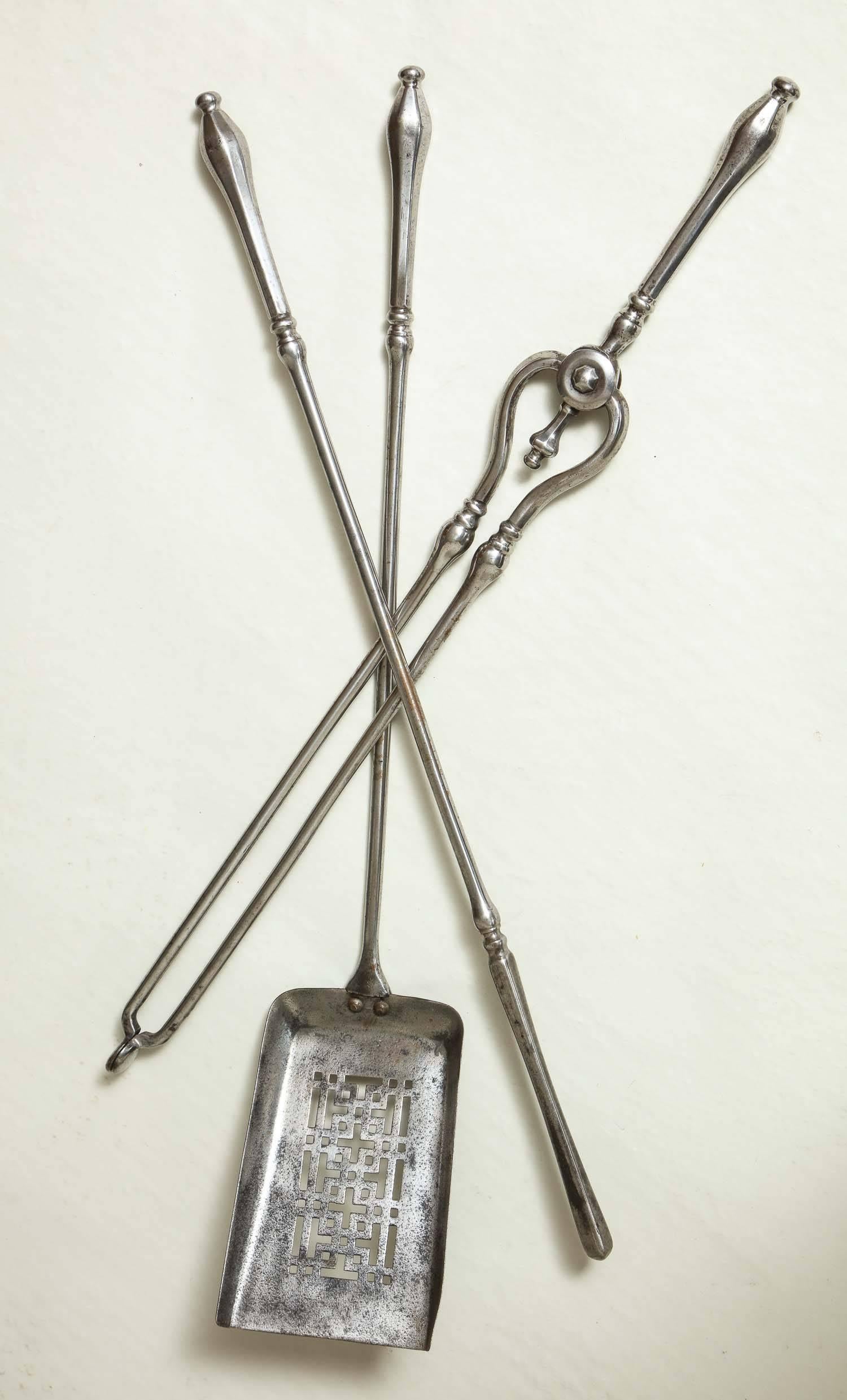 Fine set of George III period firetools in gunmetal steel with hexagonal teardrop handles, comprising a pair of tongs, poker and shovel, the latter with Chinese fretwork piercing to the bowl, England, circa 1800.