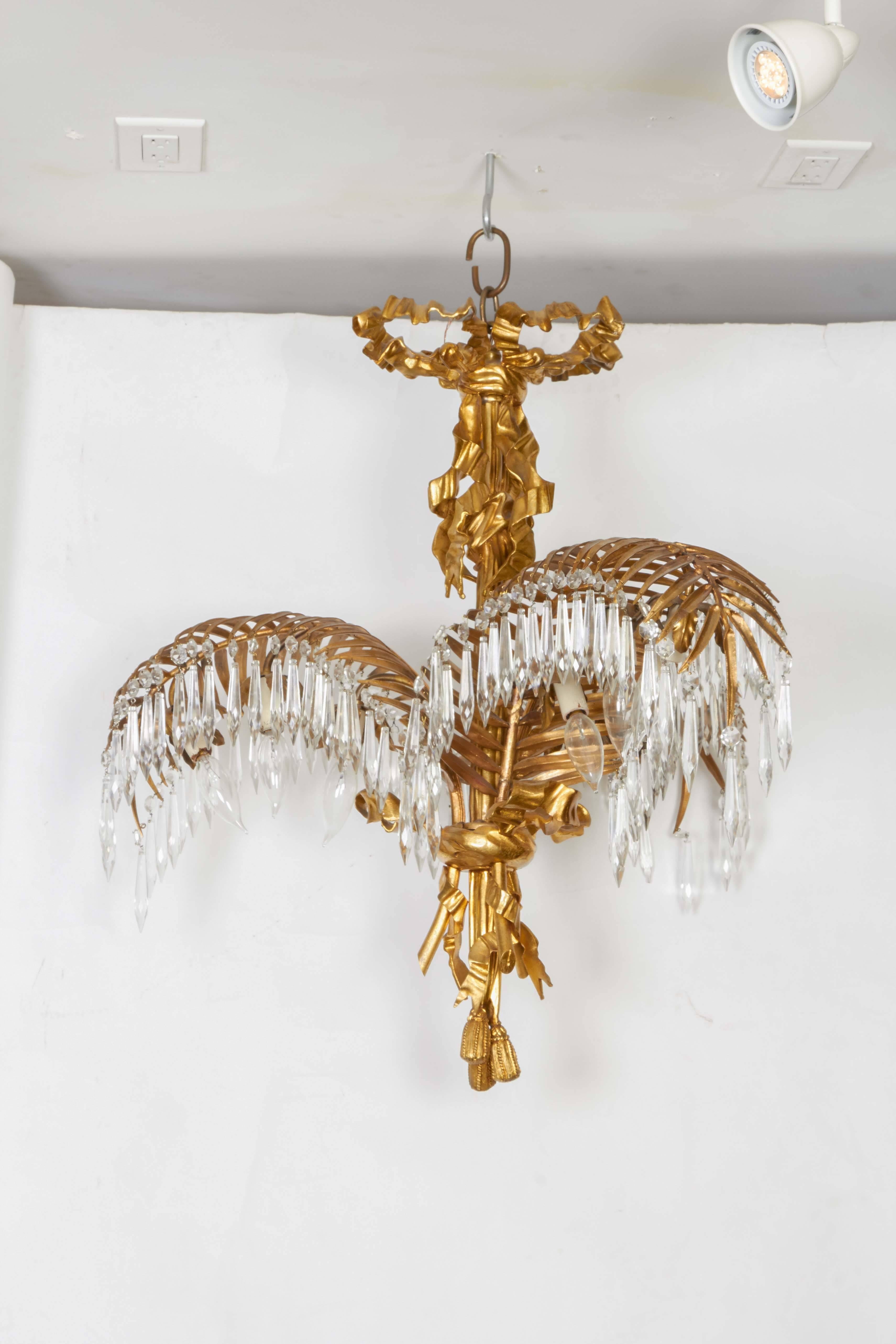 A French gilt bronze palm frond chandelier, the stem surmounted by ribbon tied spray and issuing three ornate palm branches suspending crystal prisms and concealing 9 Edison sockets (3 to each branch), with tassel finial.