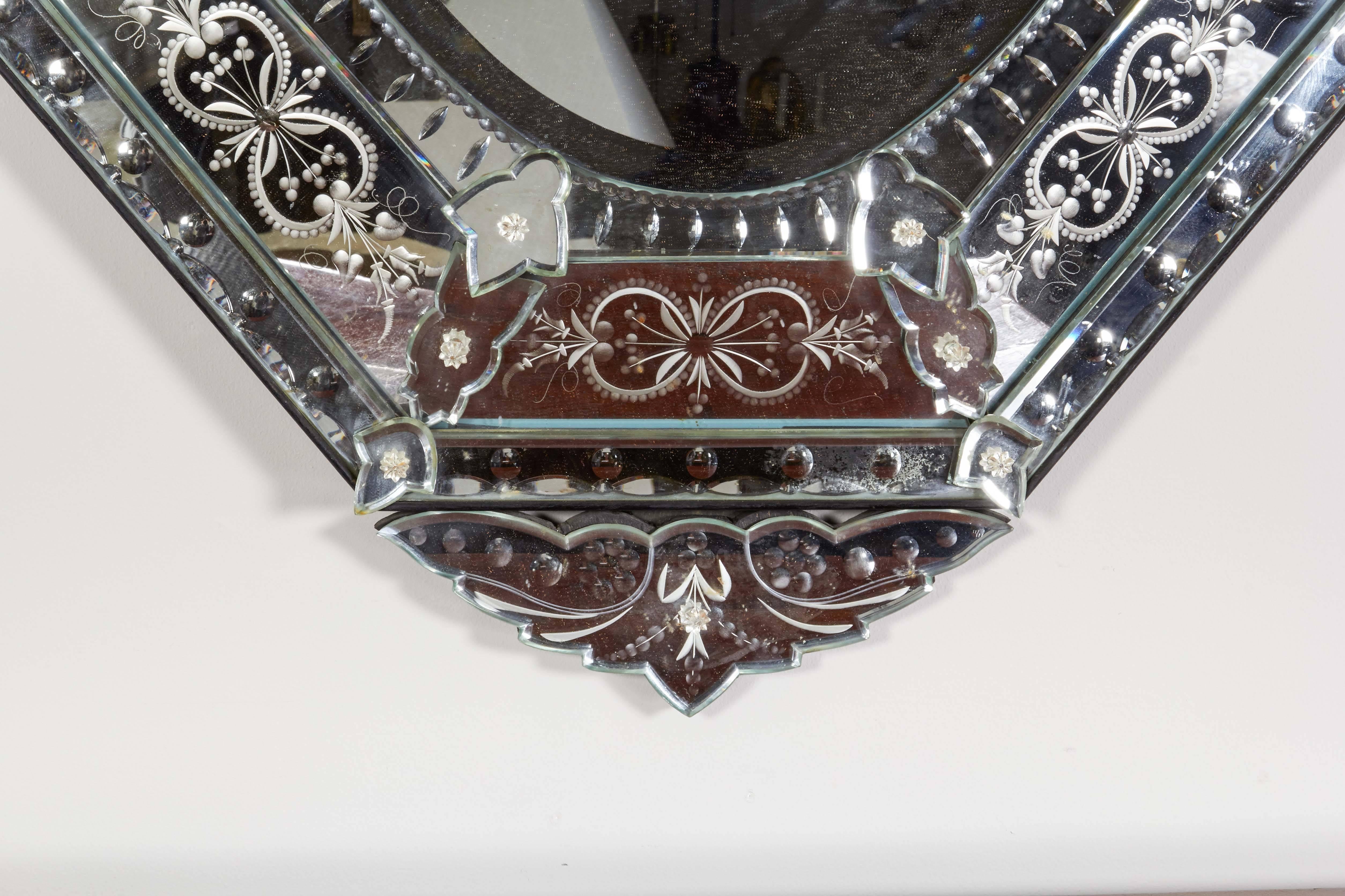 A Venetian etched glass mirror, with foliate scroll crest, the beveled glass plate having mirrored outer frame with reversed glass etching, each section secured by mirrored rosettes.