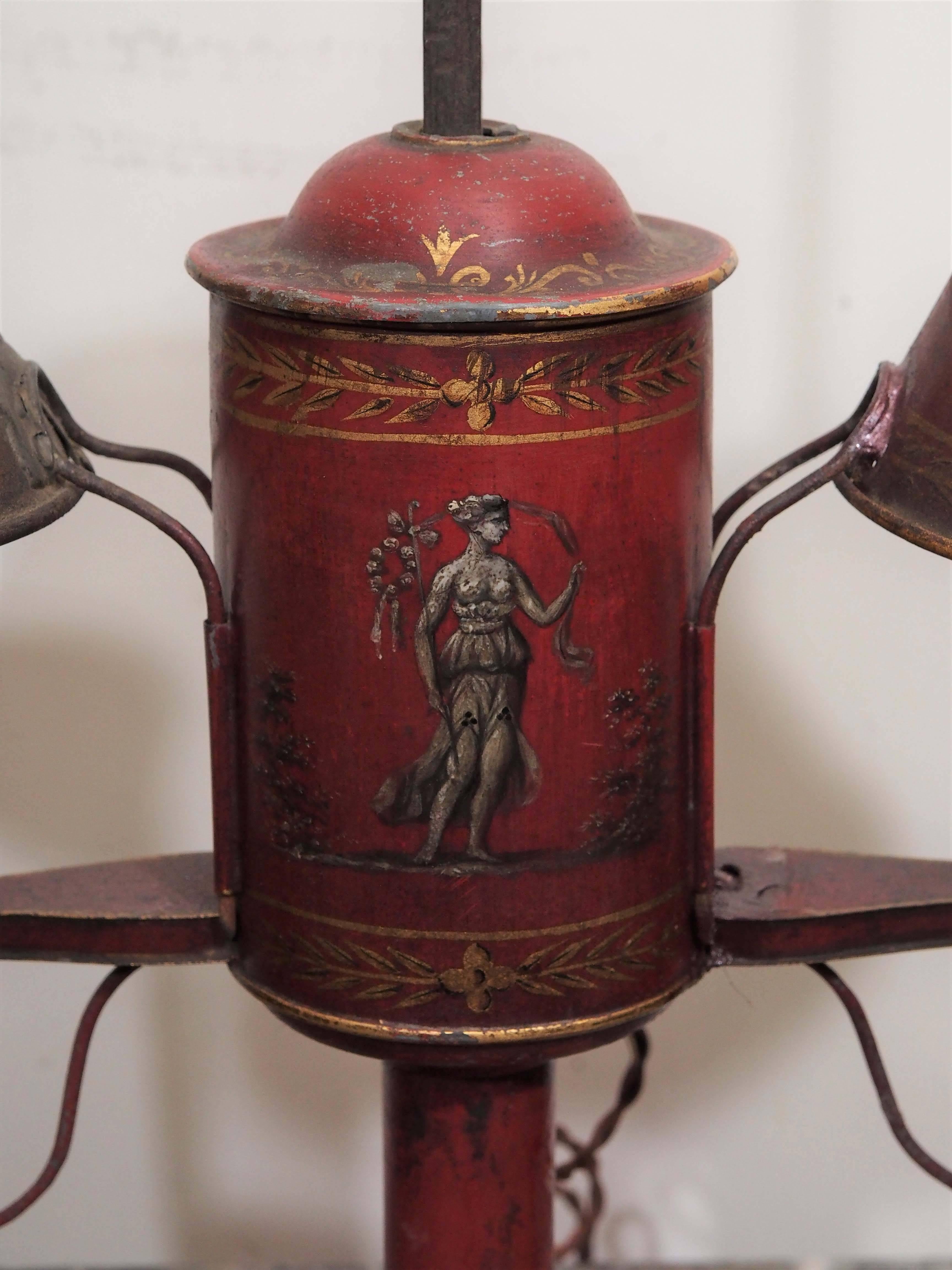 French Tole two-arm student lamp with classical scenes and red tole shades.
Adjustable central pole with flared base.