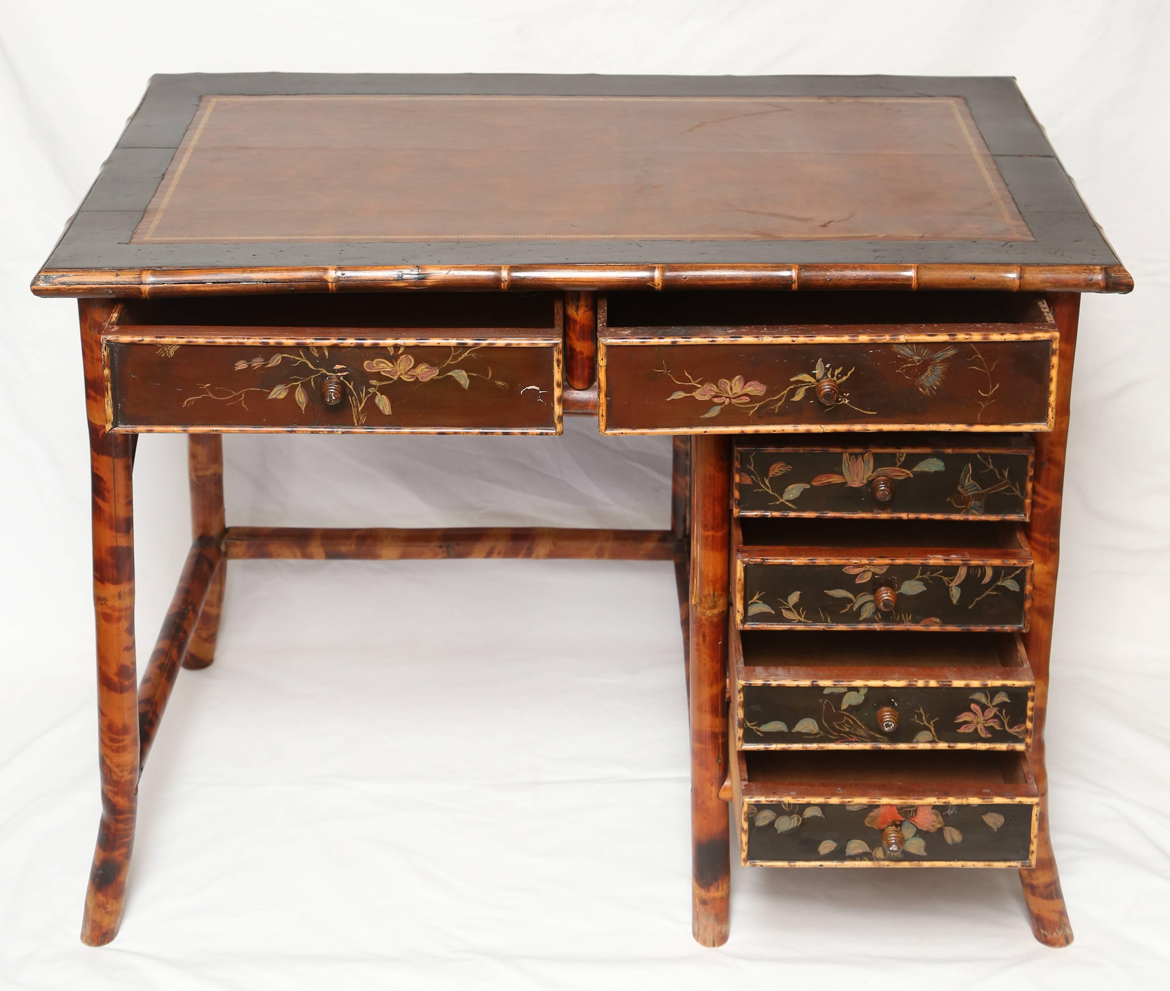 19th century English bamboo desk with hand cut dovetails, configured with two long drawers over a four small drawer cabinet, drawer panels paint and gilt decorated with birds, branches and flowers, inset leather top. Measures: 29 x 39 x 23 in.