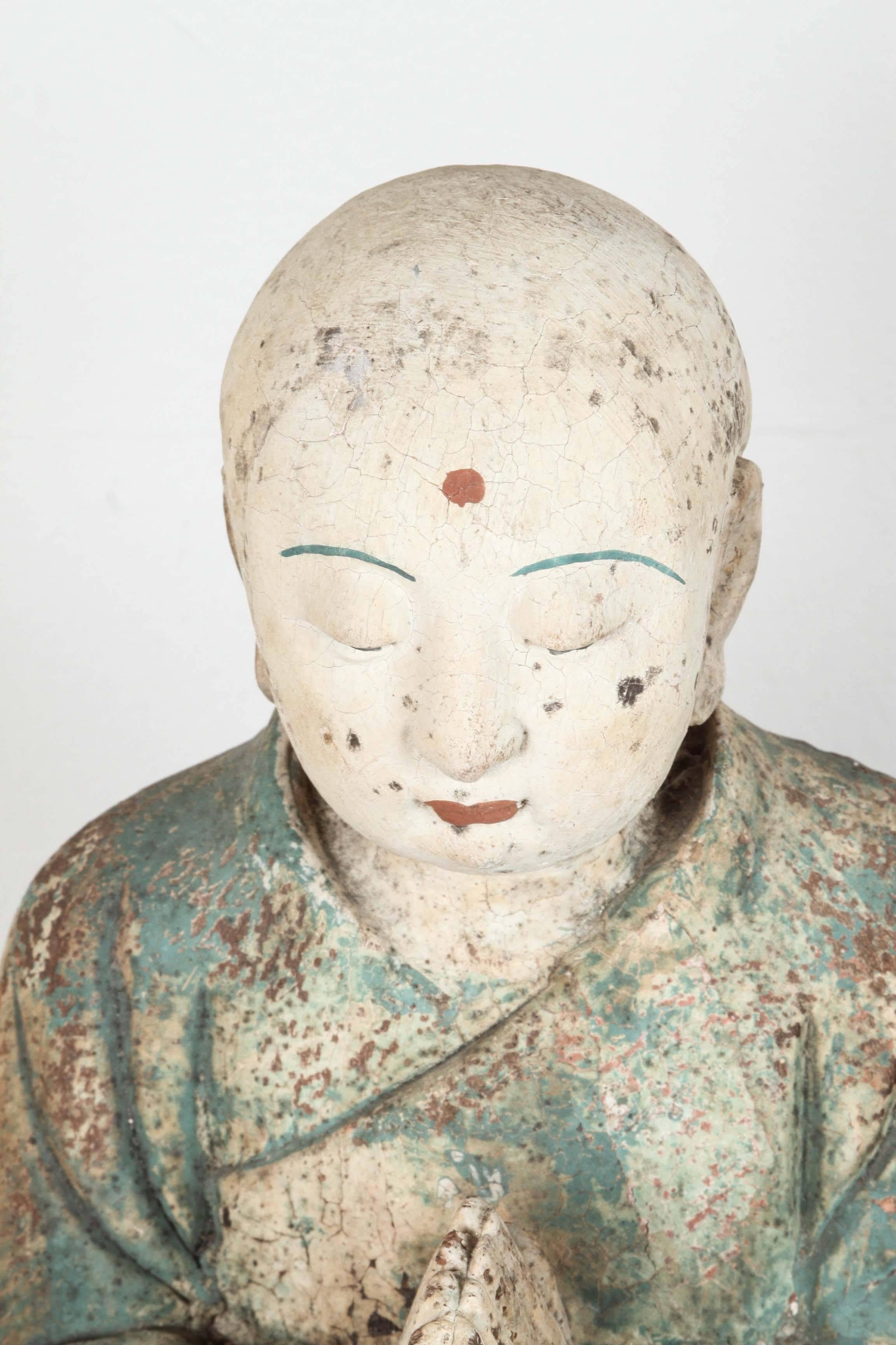 20th century hand-carved wood figure of a praying Lama or a monk. Distressed red, green-blue, ivory, black and white paint.