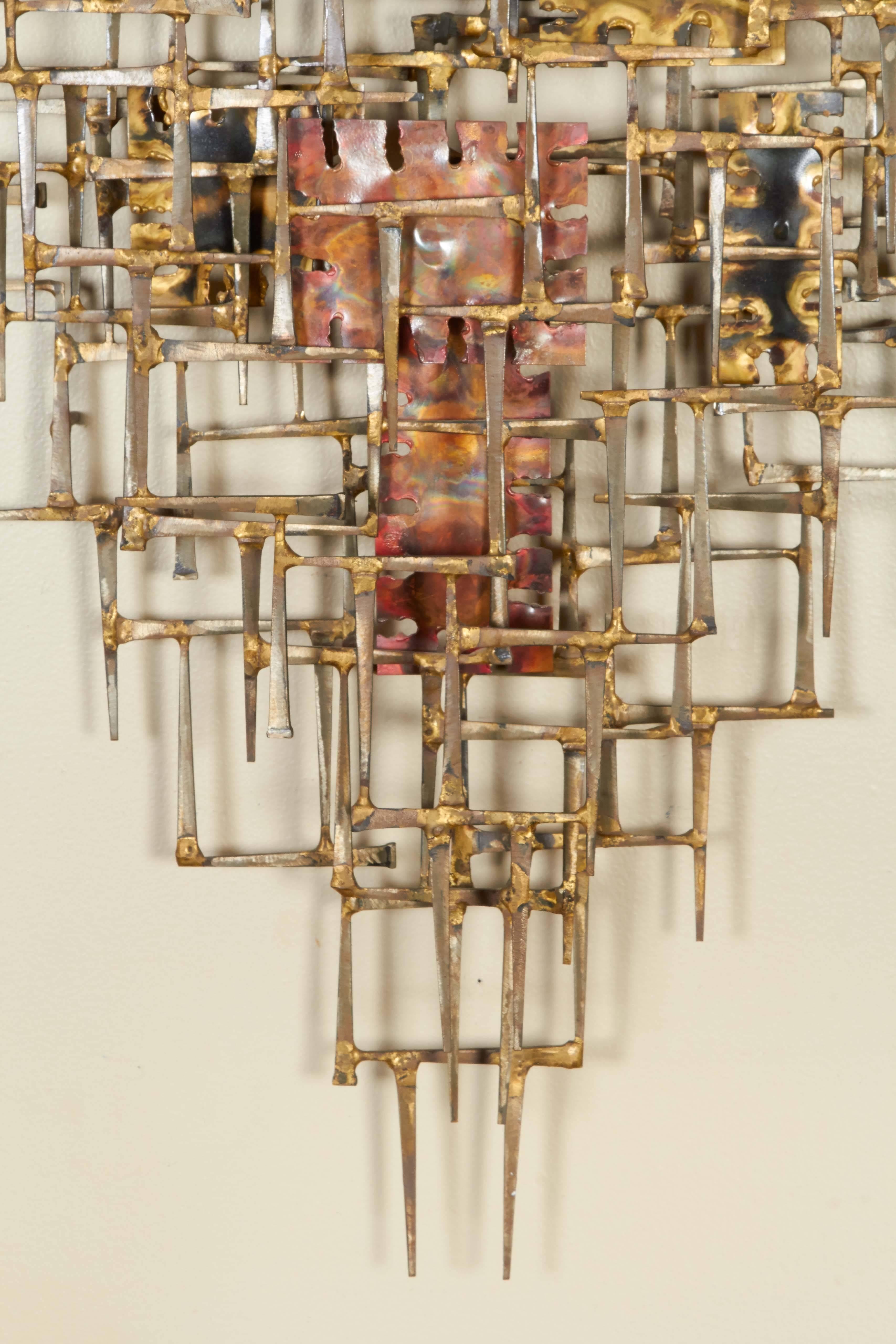 A Brutalist abstract wall mount sculpture by Silas Seandel, hand-wrought and crafted of gilt and enameled mixed metals in gold and red tones, circa 1970s. Signed Silas on the back of the sculpture. Very good vintage condition, consistent with age