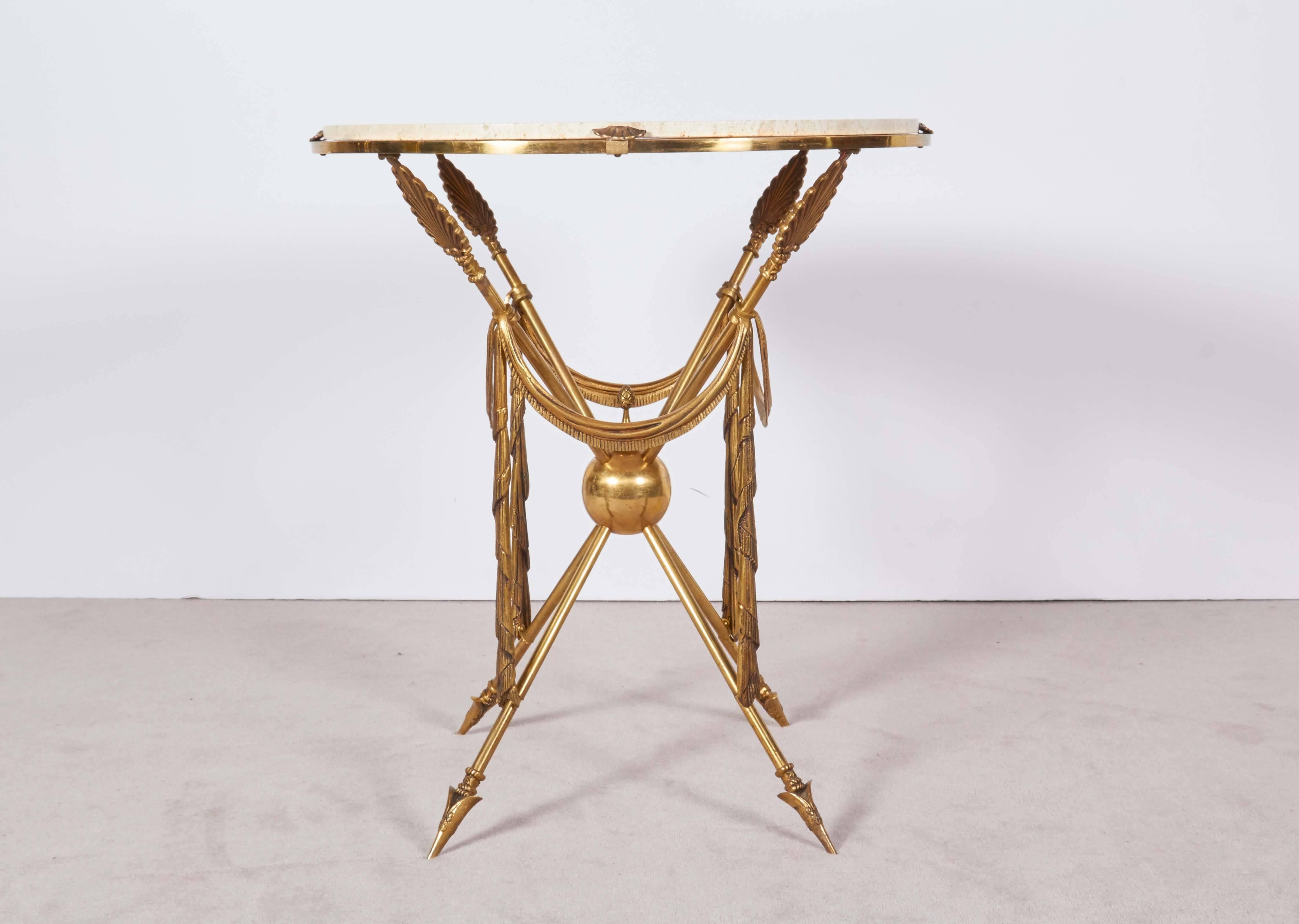 A 1970s Italian martini and cocktail table, round travertine top on brass base featuring four crossed arrow motif legs, with anthemion vanes, terminating in arrowheads, joined at the center by brass ball with pine cone finial and festive swags. Very