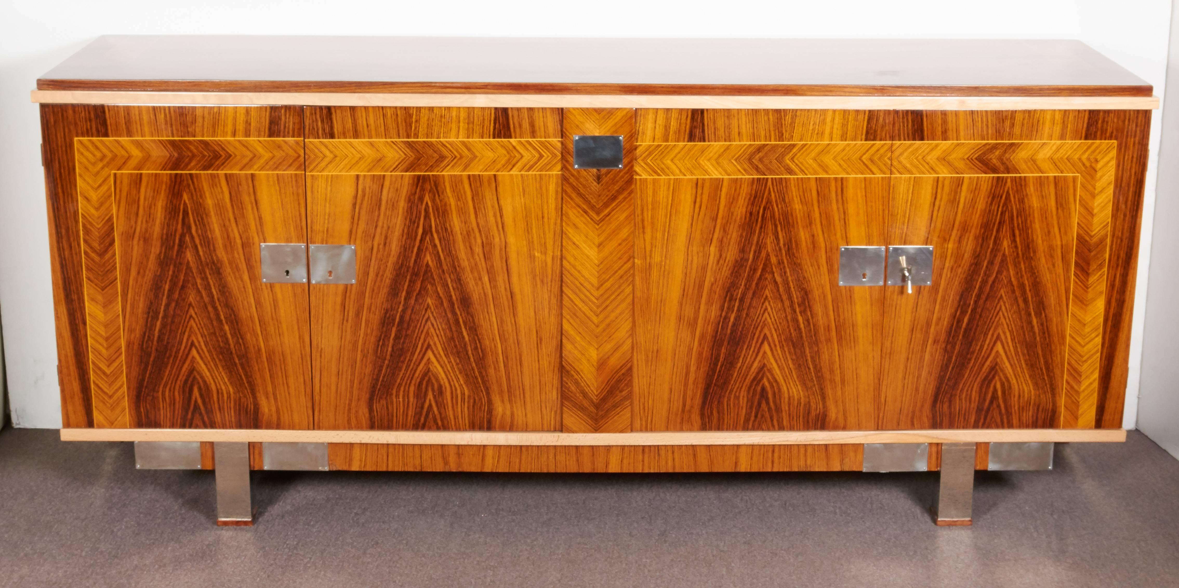 A French Art Deco four-door sideboard featuring beautifully grained exotic rosewood with blonde trim and parquetry detail, along with sleek nickeled bronze hardware. The cabinet is supported on a tall back tubular leg with matching short cube front