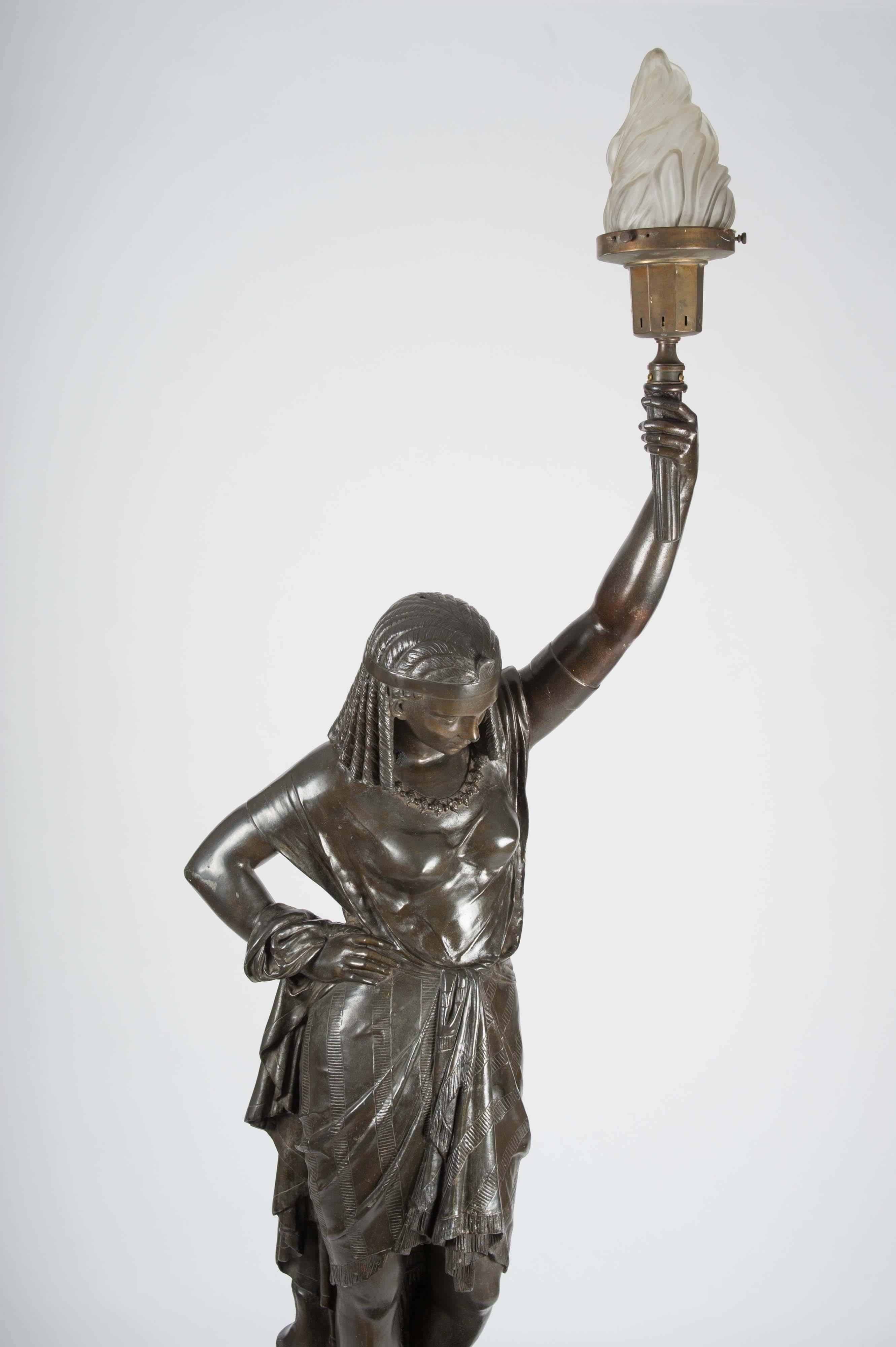 This French bronze sculpture depicts an Egyptian female holding a light in the form of a torch, which would have originally been a gas light. It is a smaller but identical version of the lifesize bronze we have on another listing. The sculpture is