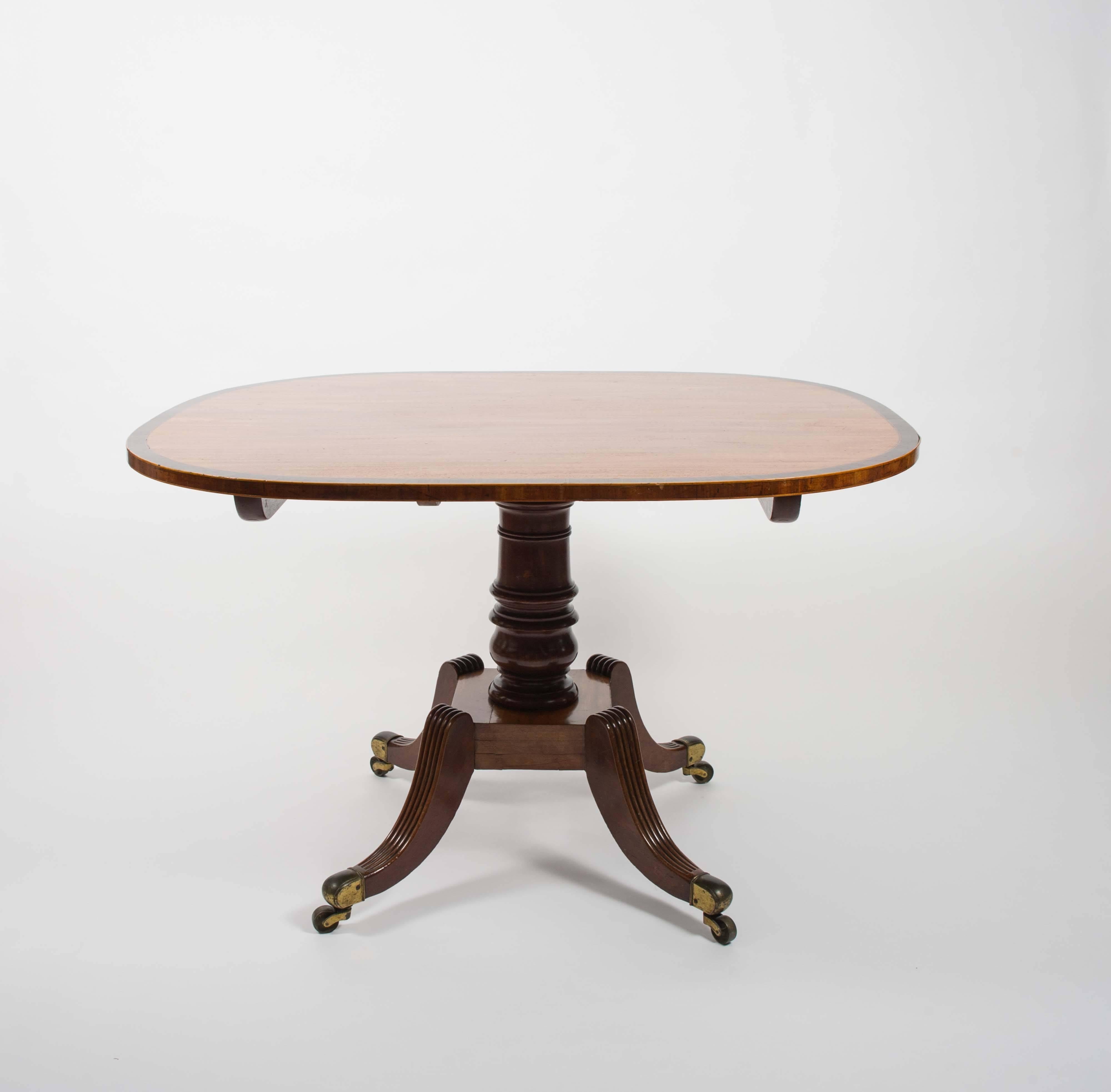 This very attractive and versatile sized English mahogany Regency tilt-top breakfast table features a lovely rosewood crossbanding border with a rectangular shaped top and rounded corners. The table is supported on a central column and Quadra form