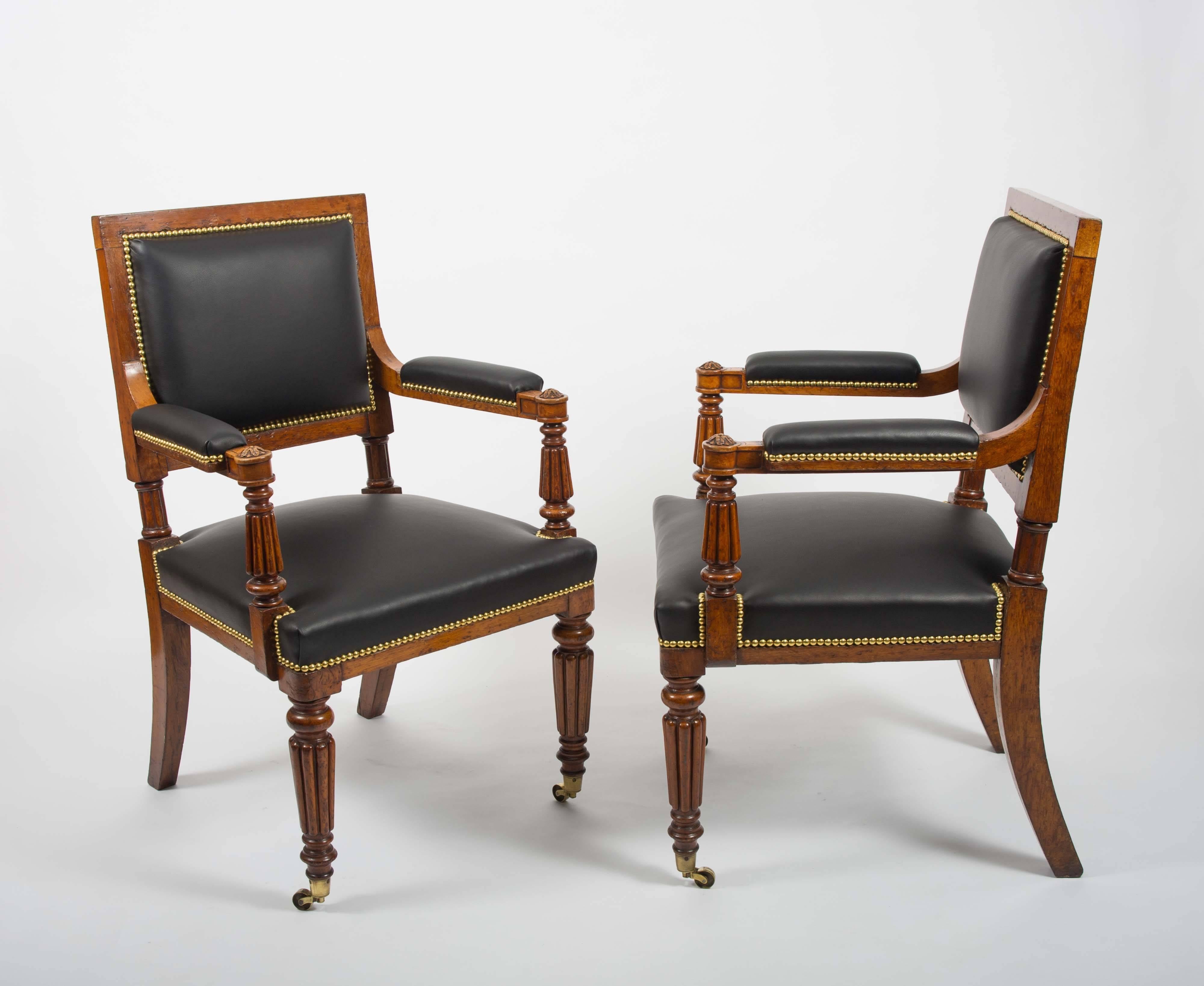 This gorgeous and superb pair of English oak elbow chairs feature swept back and front reeded legs on brass castors. They are upholstered in black leather with matching leather armrests and trimmed in brass stud detail. Each chair measures 24 ¼ in –