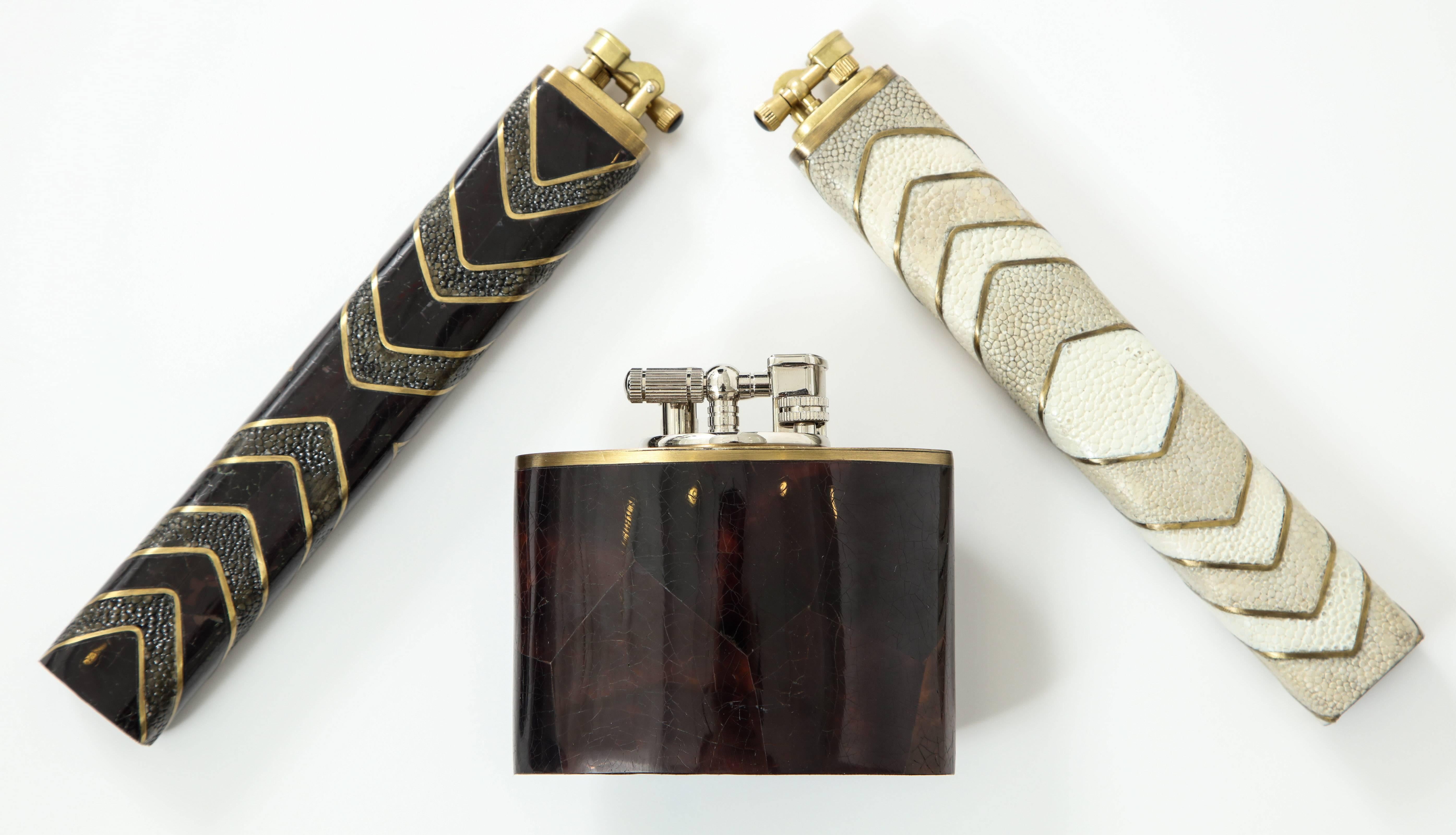 Shagreen lighters with decorative details of black sea shell, both priced at $495 each. Oval lighter made of dark brown sea shell, priced at $495.