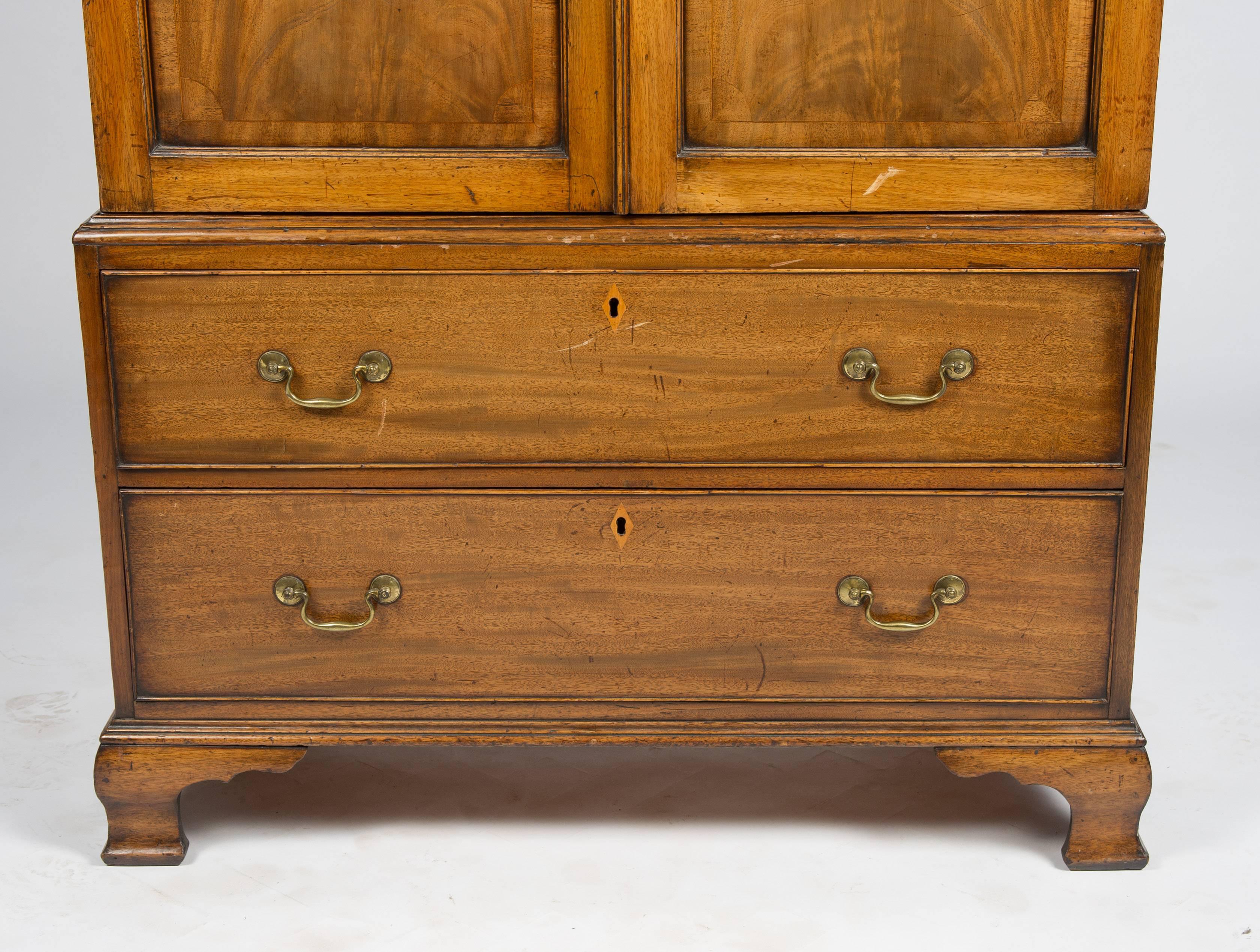 A good quality Georgian period mahogany linen press, having a swan neck pediment cornice, with carved paterae and inlay, with dentil moulding. The pair of doors open to reveal hanging storage space (lined in fabric). Two deep drawers each with their