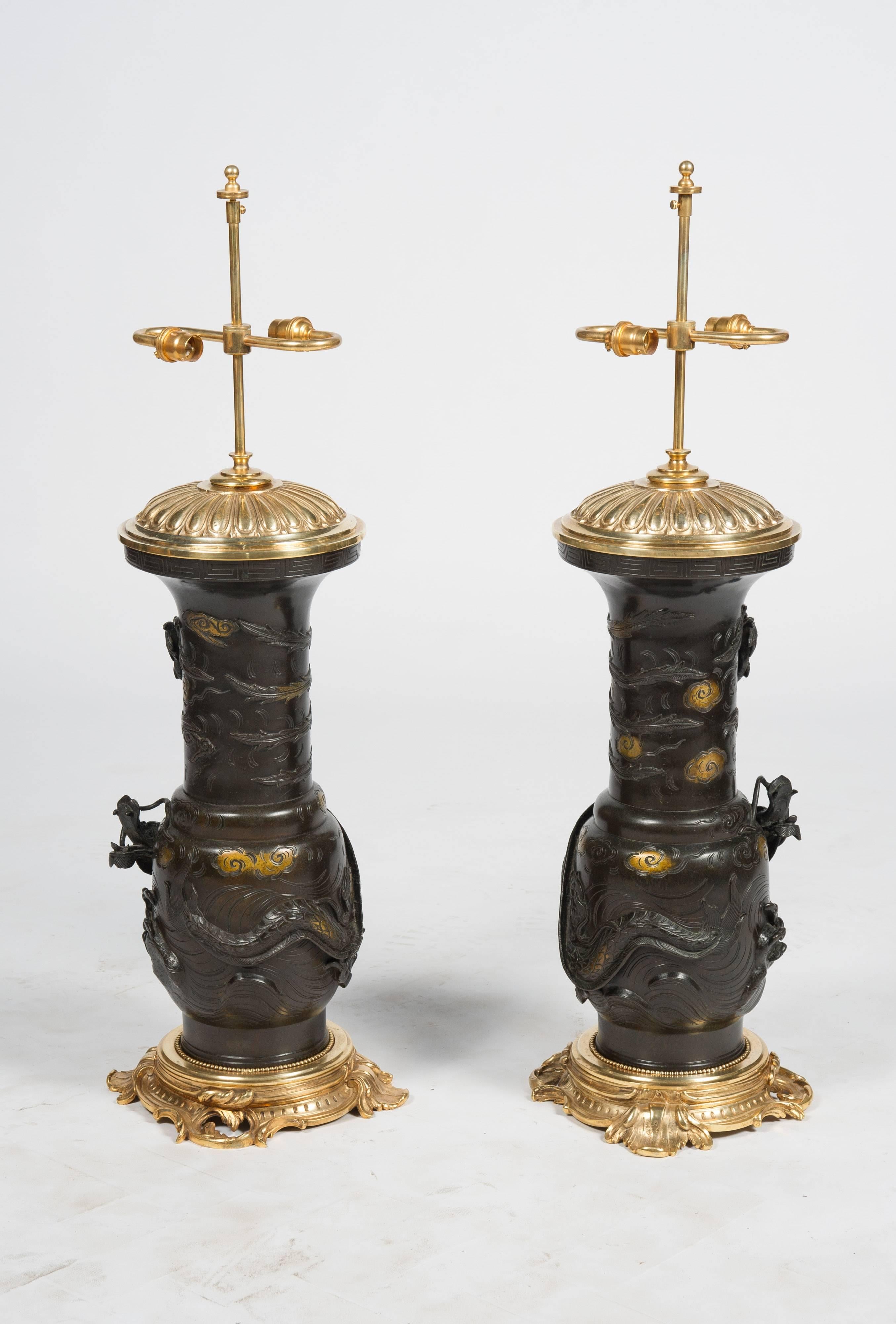 Une paire très impressionnante de vases en bronze du 19ème siècle, de la période Meiji (1868-1912), chacun avec des dragons mythiques enroulés autour d'eux, rehauts dorés. Montés sur des socles et des plateaux de style rococo en bronze doré.