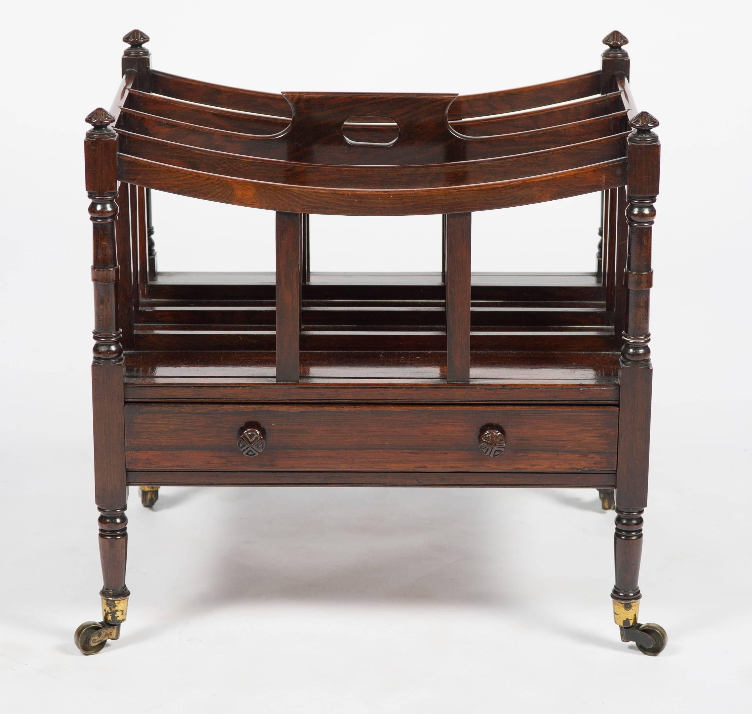 A very good quality Regency period rosewood canterbury, having three internal divisions with a fretted handle to the centre. Turned finials to each corner, a mahogany lined frieze drawer with a pair of handles, raised on turned tapering legs,