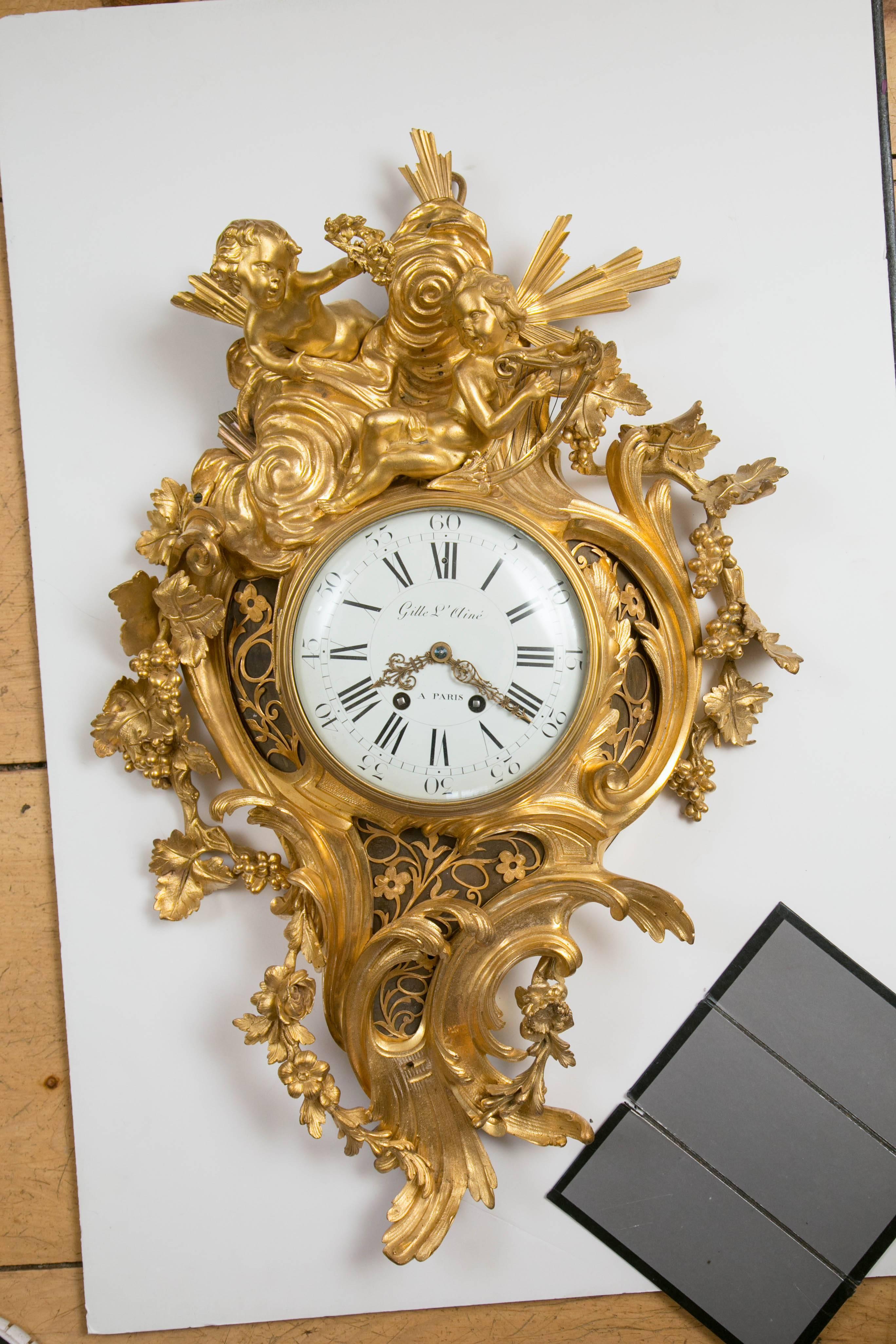 Fire gilt bronze in the rococo style with two putti atop. One putto is playing a harp while the other holds aloft a wreath. Sun rays emanate from behind them. Scrolls, leaves and flowers complete this beautiful Cartel. The clock face is signed Gille