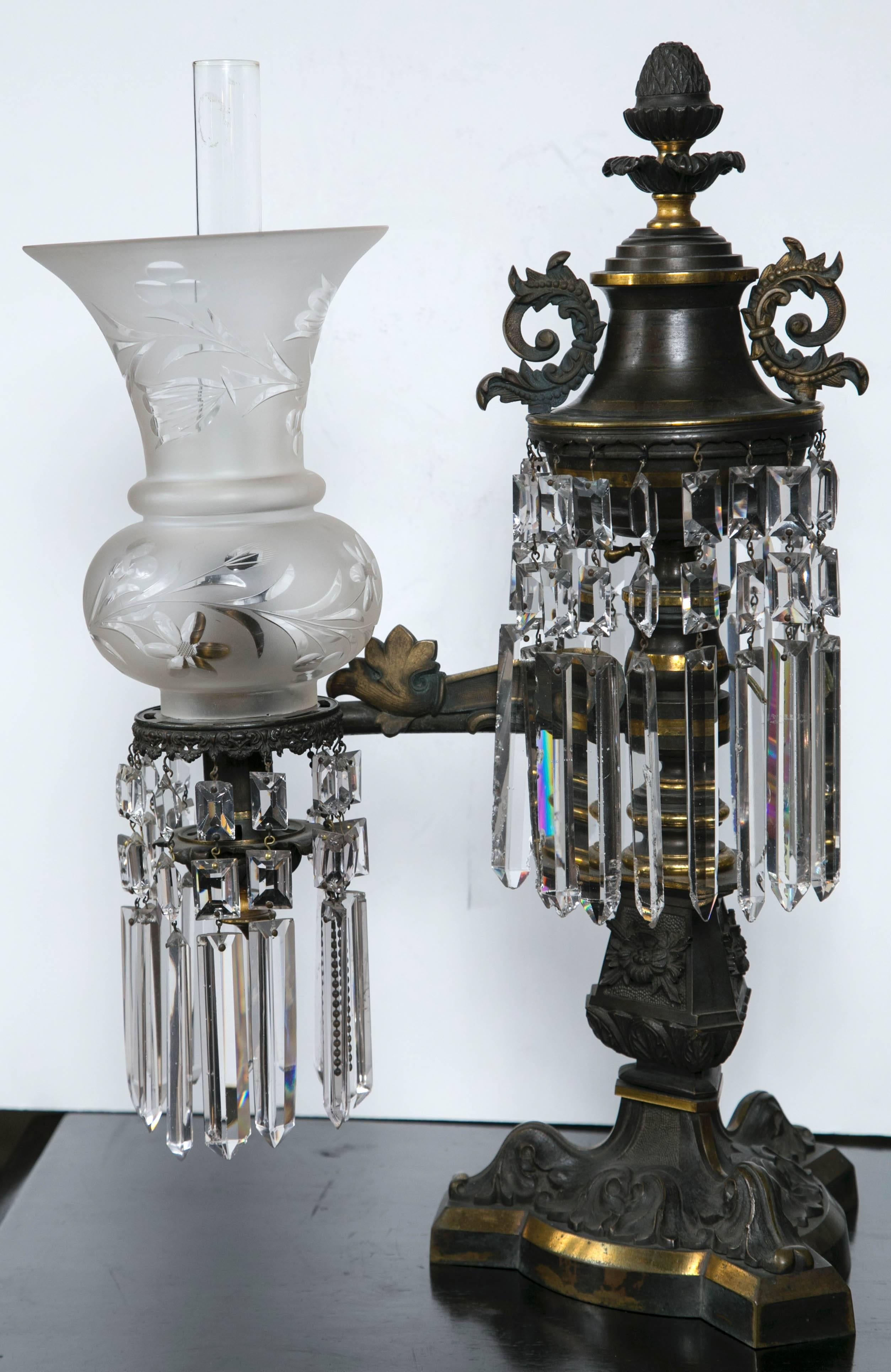 This pair is unsigned, but of high quality cast and chased bronze. There is a narrow hurricane shade wtihin the flared frosted and cut-glass outer shade. Scrolls of acanthus leaf and other designs, with an acorn finial atop. Some drop crystals might