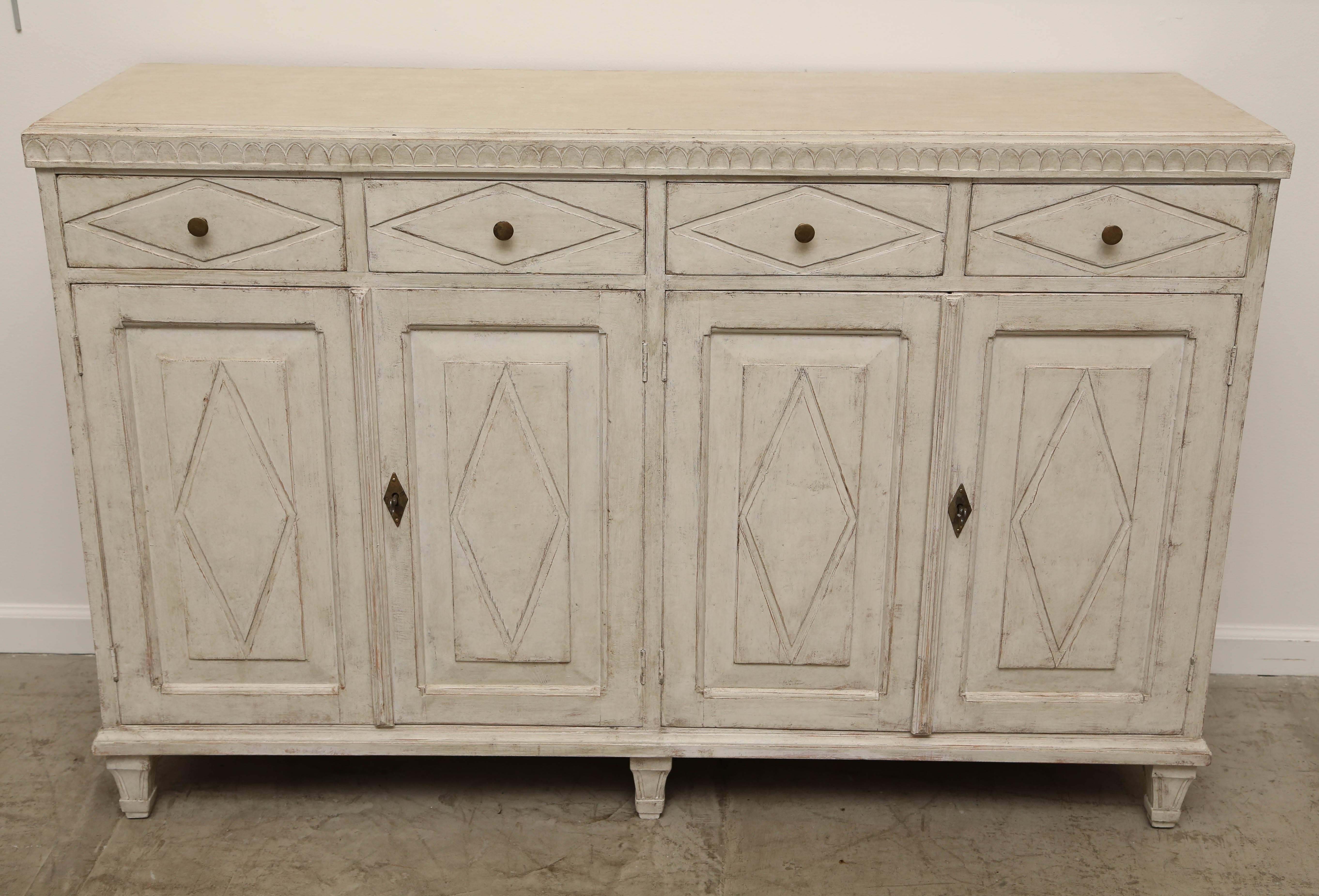 Antique Swedish Gustavian Style painted four-door sideboard with four diamond shaped doors and drawers with lambs tongue moulding beneath top, one interior shelf.  The paint has been refreshed in traditional distressed Gustavian white. Original