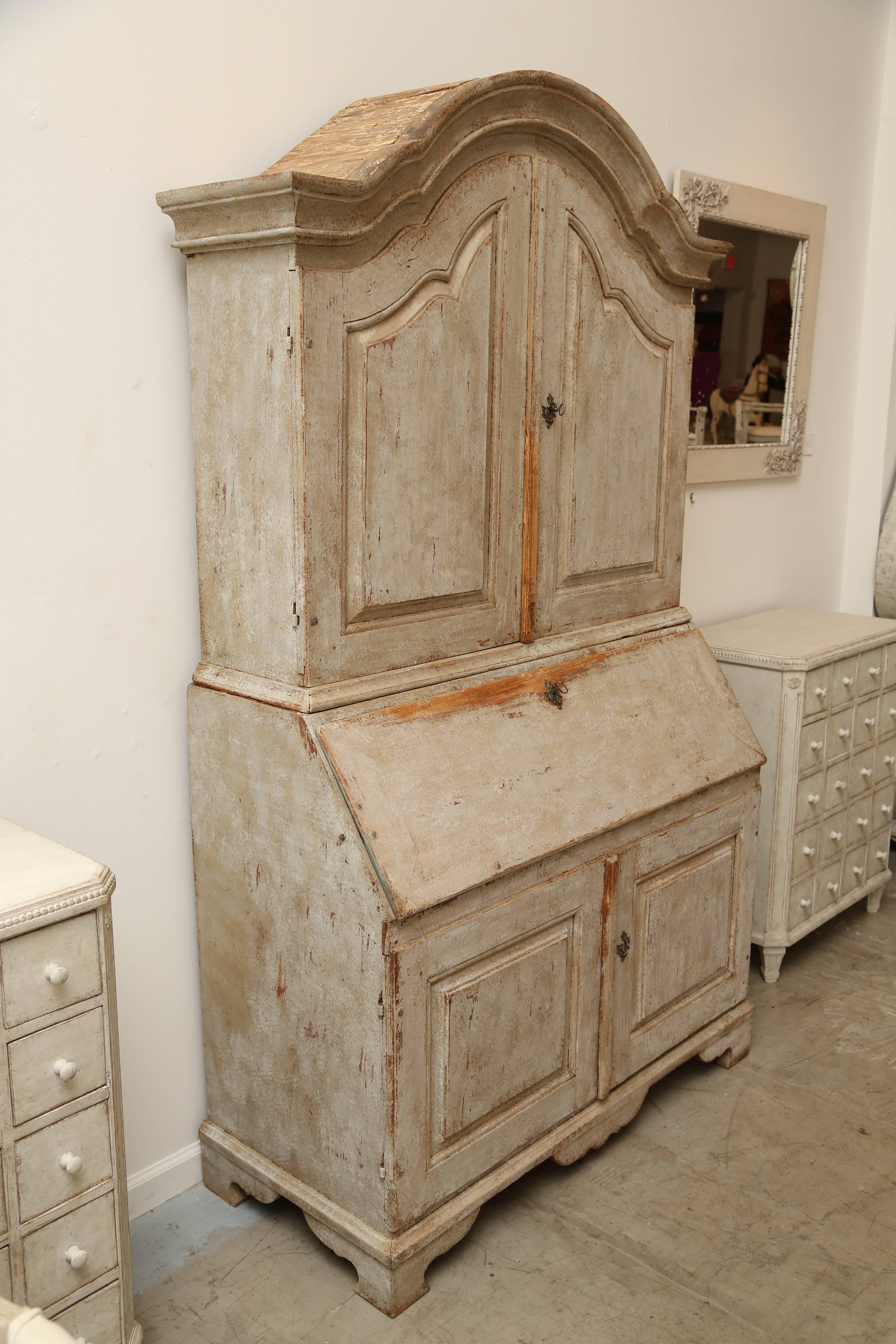 This Baroque secretary has a lovely distressed painted finish in greenish beige exterior and a greenish blue interior. 
The arched cornice starts at the top. Once the doors are opened, there's a curved shelf with spoon notches and three shelves