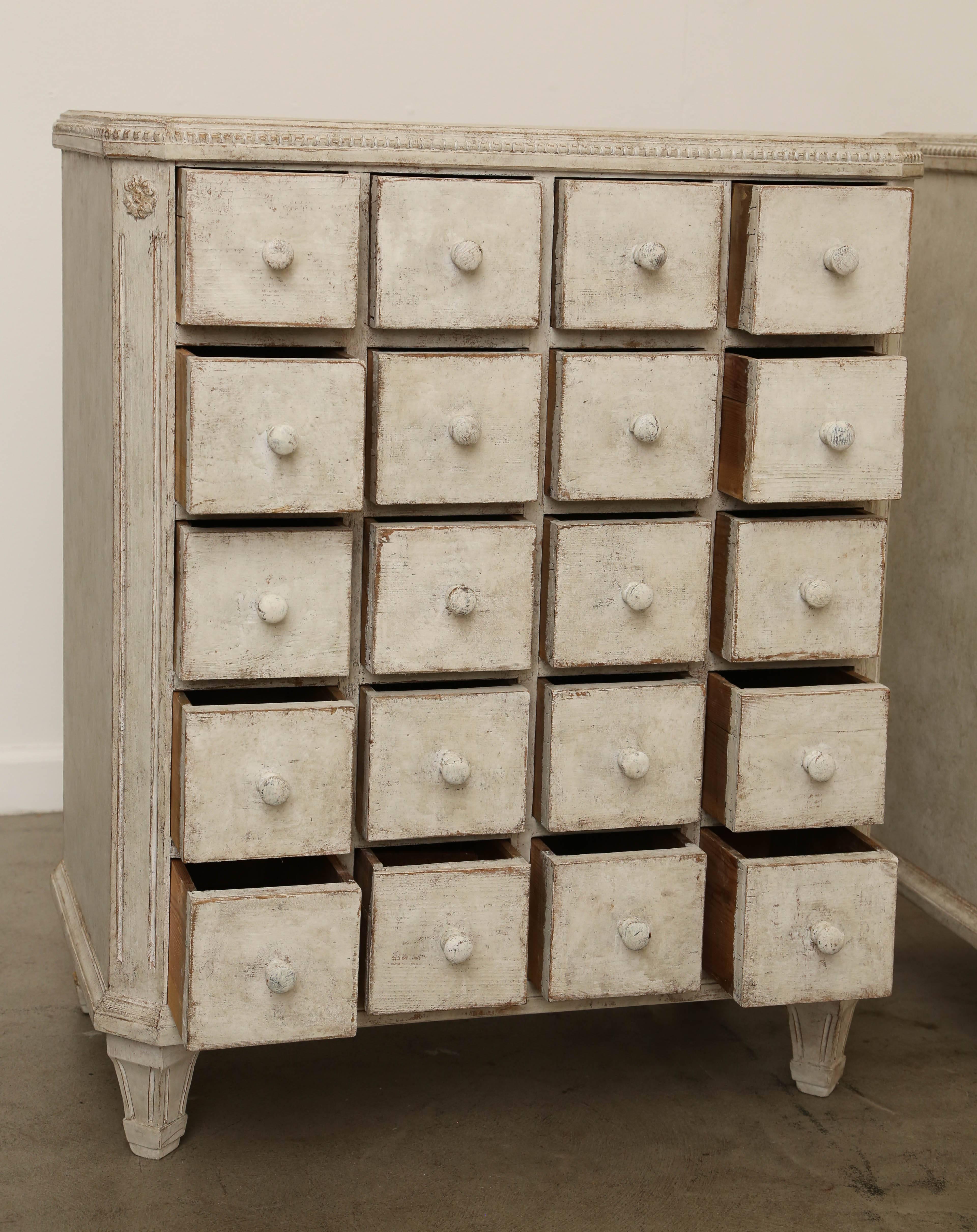 One antique Swedish Gustavian Style painted apothecary chest which is rare and unusual. Painted in Gustavian white with a subtle green undertone. Beaded border top. Distressed paint finish.
Slanted corners with rosettes and fluting with tapered
