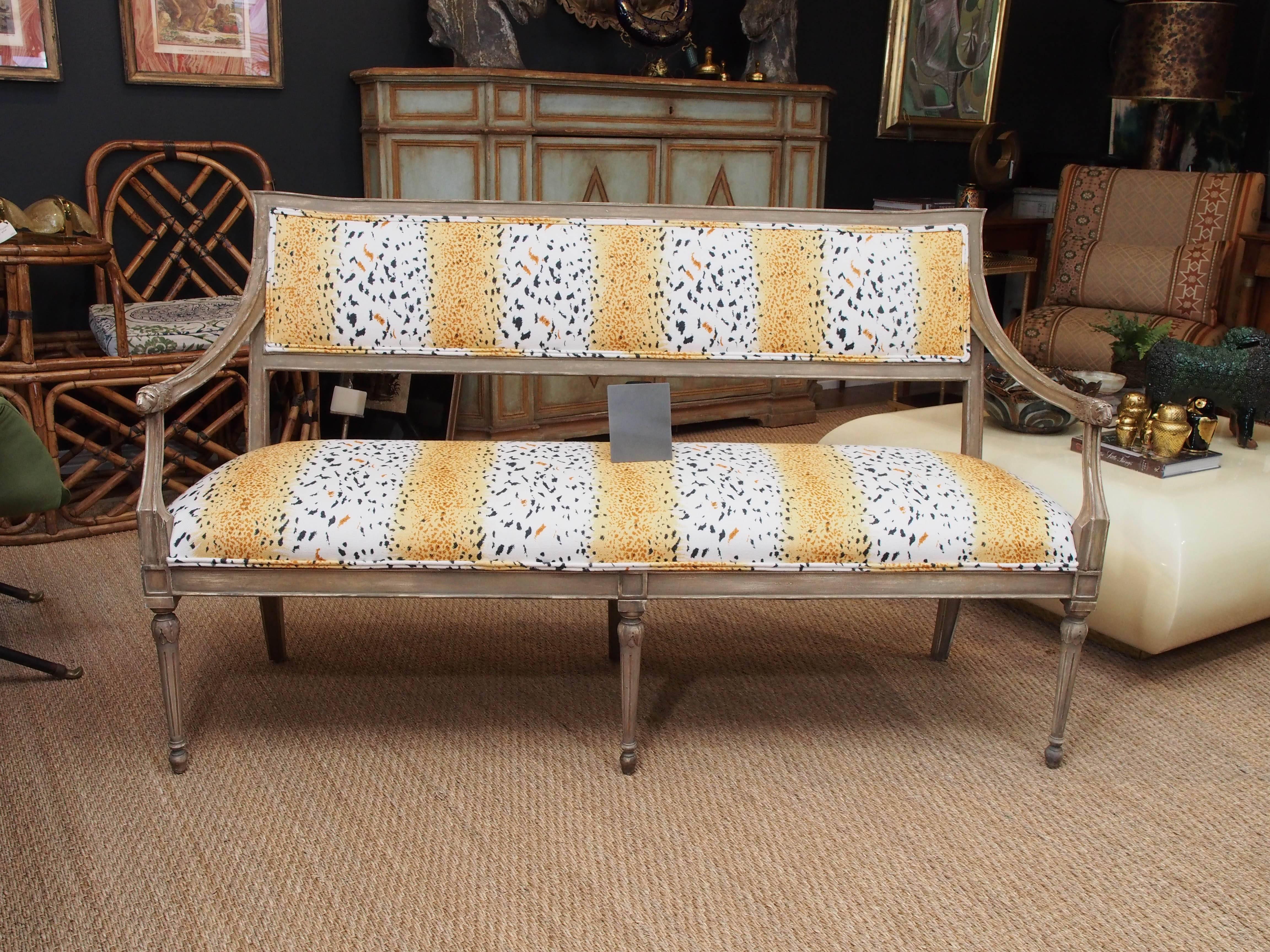 This French Provincial settee is hand-carved with lion's head handles. Angular framed back with sweeping arm and rest supports, carved details and fluted legs. Covered in animal print linen.