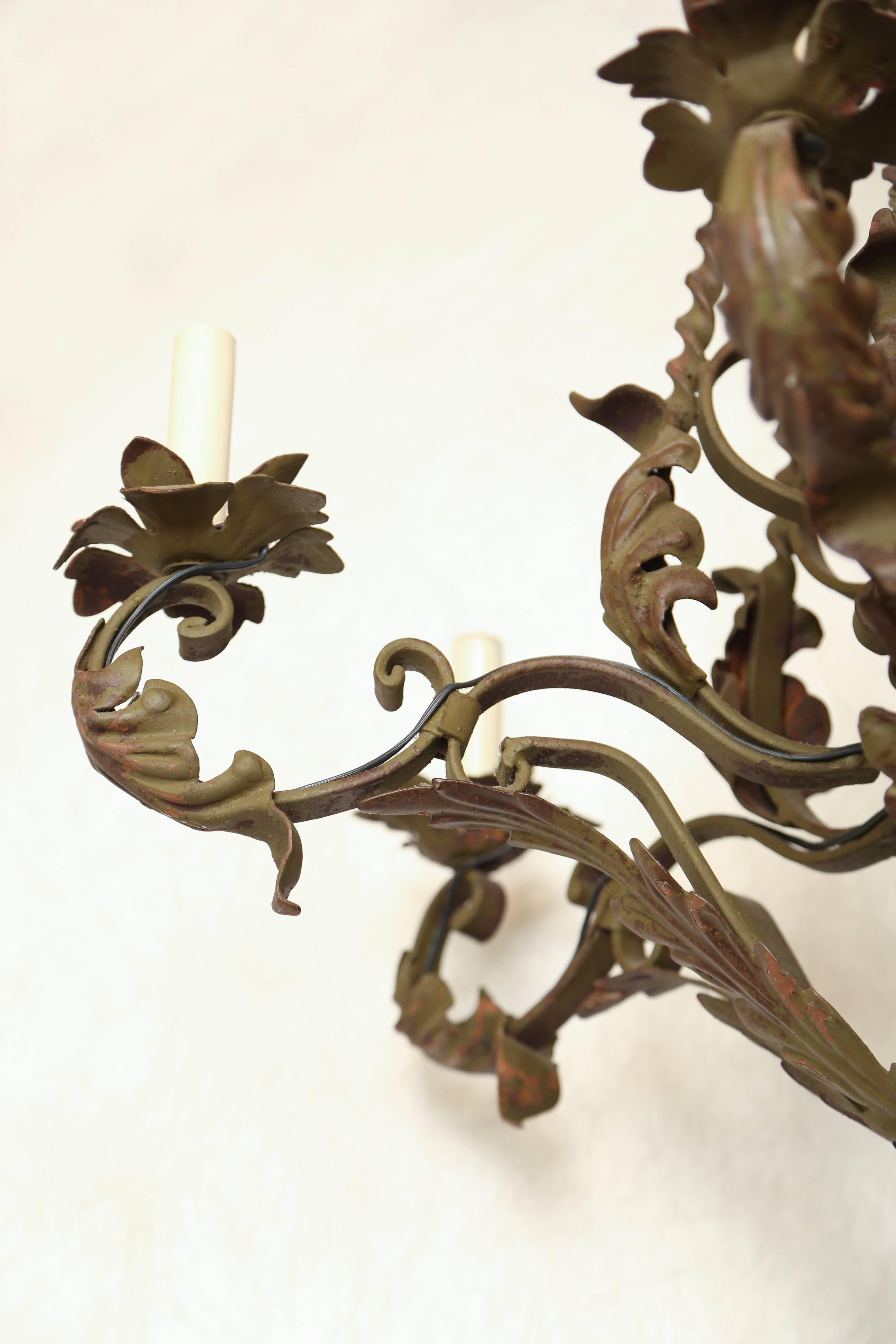 Chandelier, of wrought iron with verdigris finish, having a foliate frame of six C-scroll candlearms, ending in leafy bobeches, suspended by a frame of spiral turned iron, surmounted by a crown.

Stock ID: D8332