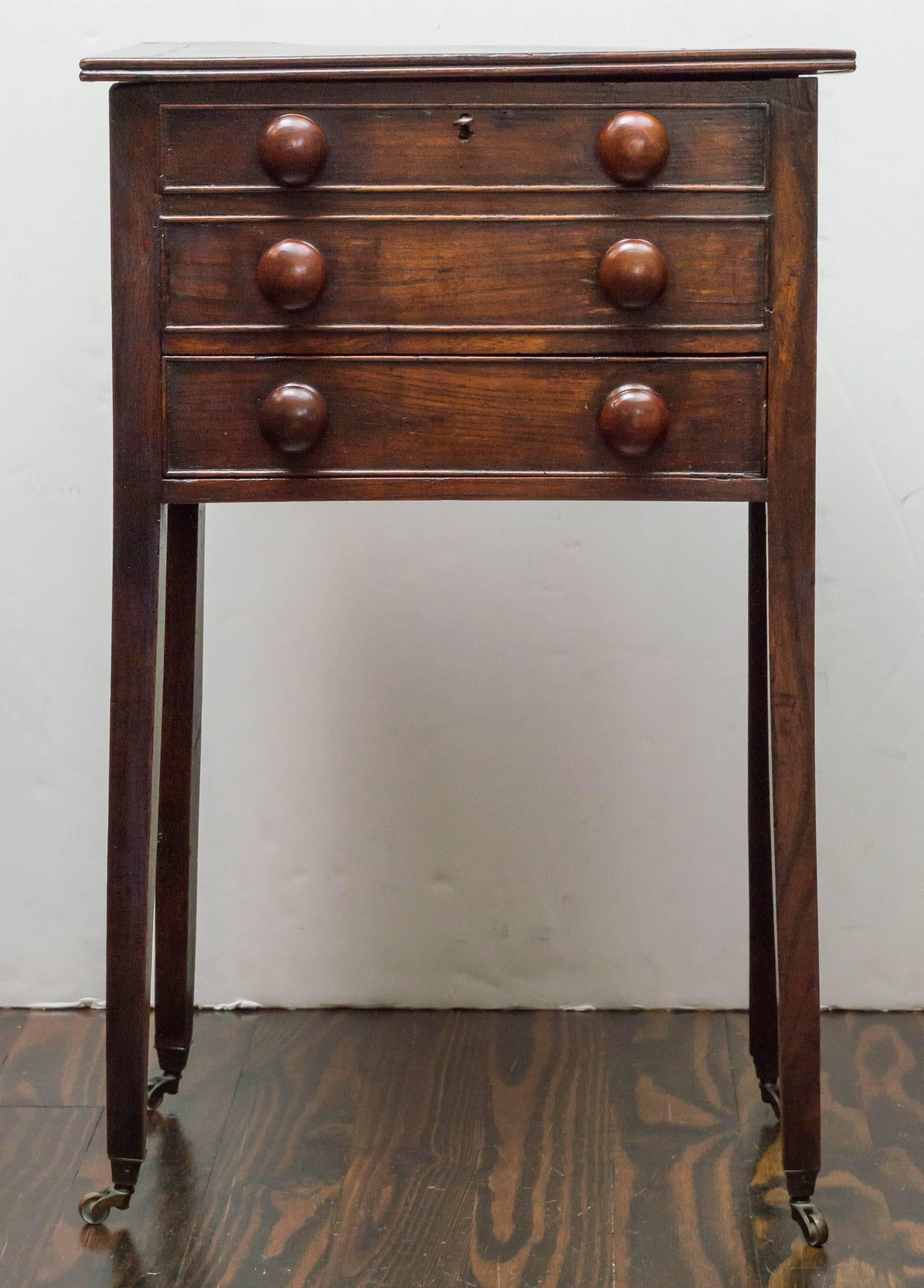 Late 18th century Georgian oak side table / stand. Perched on petite brass casters of a later date. Interesting locking bin top with a drawer below. Retains the original turned wood knobs. Deep color / undisturbed surface brought up by wax. Very