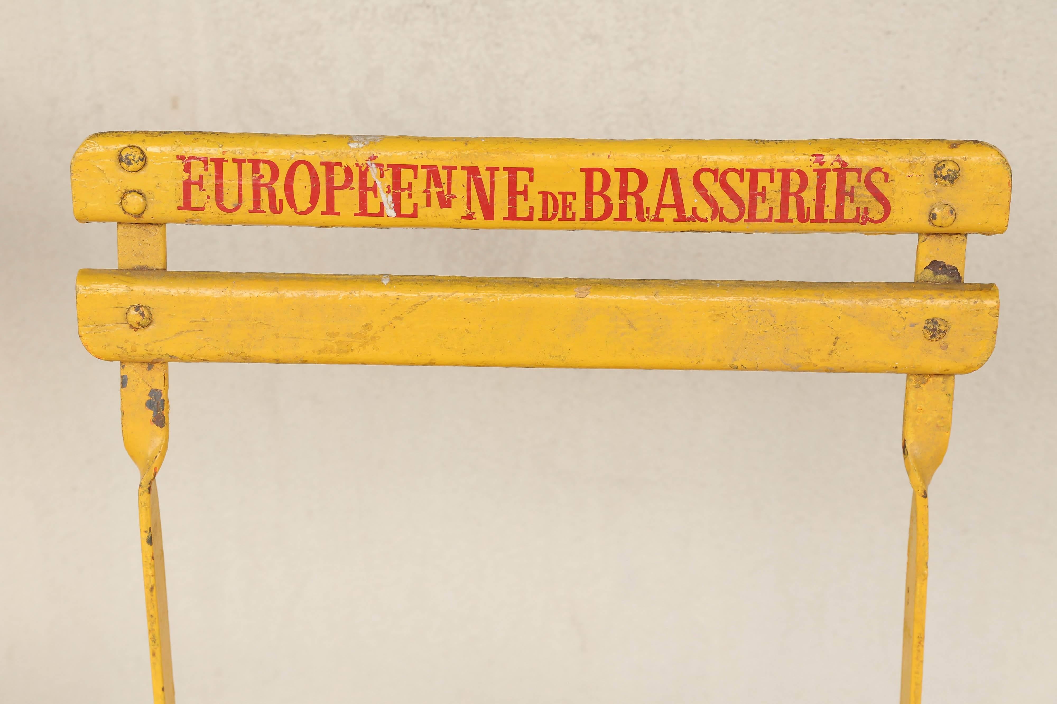 Originally used as Brasserie seating in a Paris cafe, these sturdy folding painted wooden and metal chairs can be used indoors or out. Painted a deep yellow and each has painted "Europeenne de Brasseries" in red on the back and offer a
