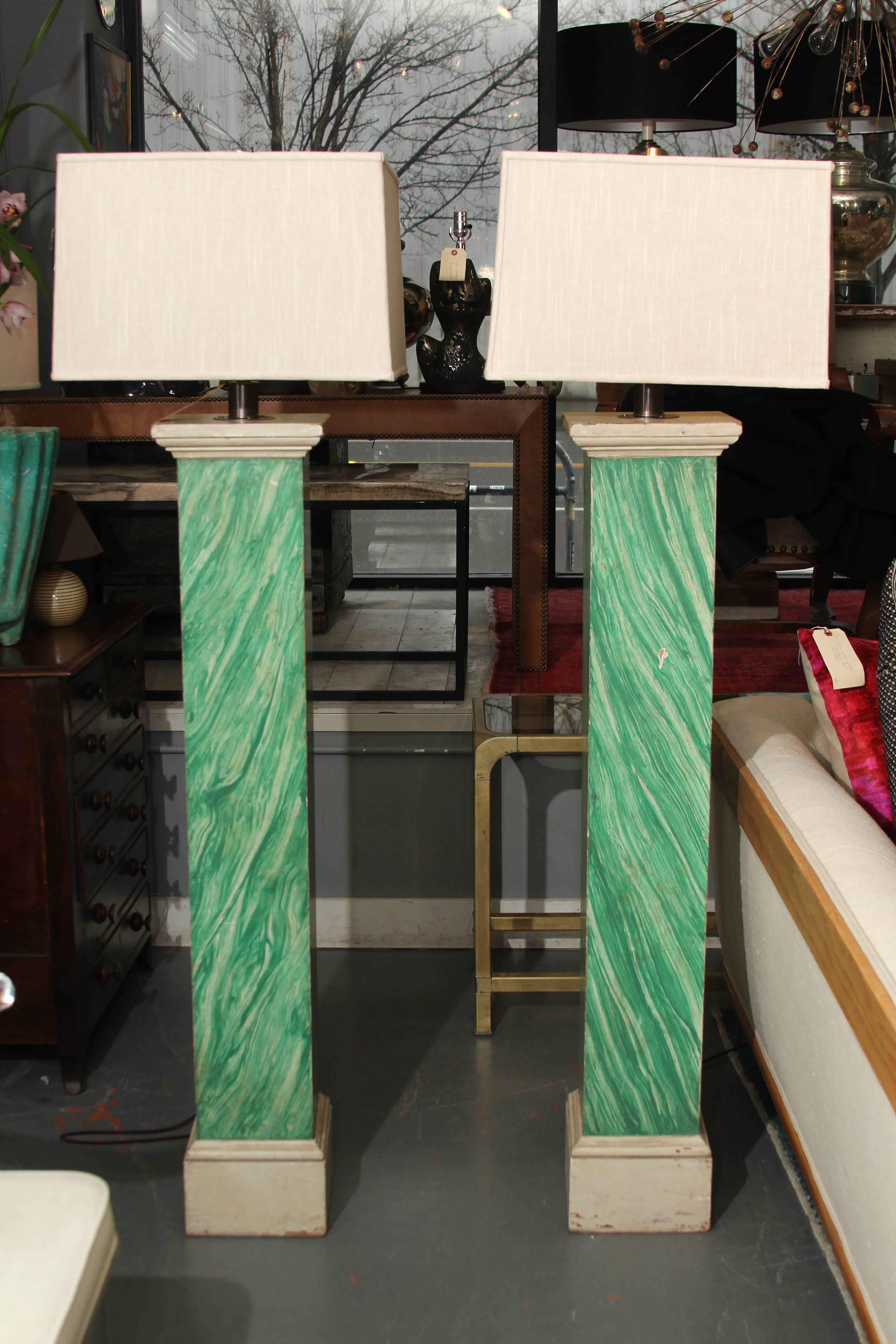 Pair of 1910 wood columns faux painted malachite wired as floor lamps. Measures: Columns are 8 1/2 x 8 1/2 in at base. Linen shades measure 17 1/4 wide at top, 18 at base, 12 in tall. Simple brass finials.