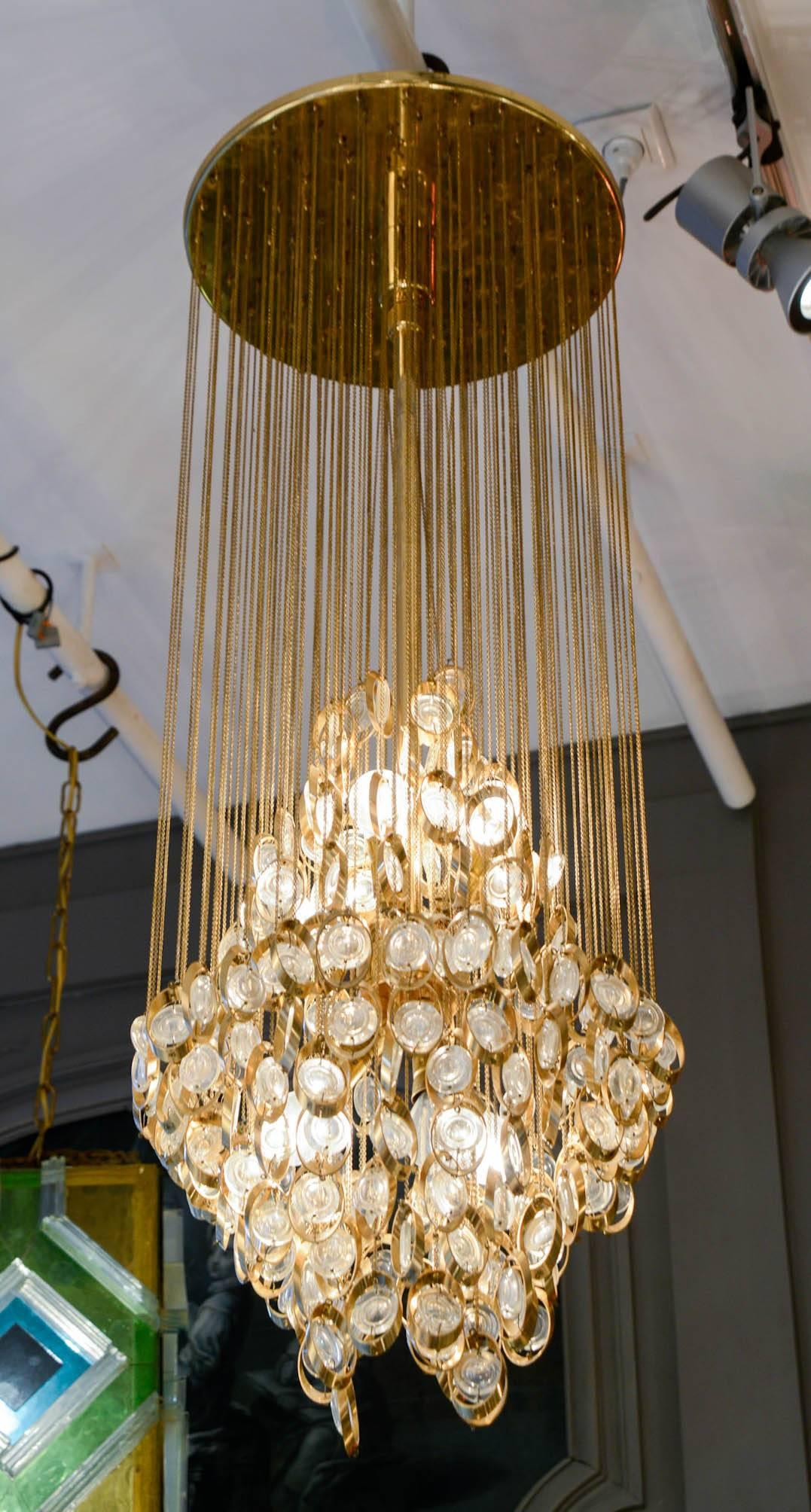 Nice suspension made of a circular plate from where hangs tens of thin chains attached to brass rings set with glass lenses. The overall is making an interesting pattern hiding the lights.
