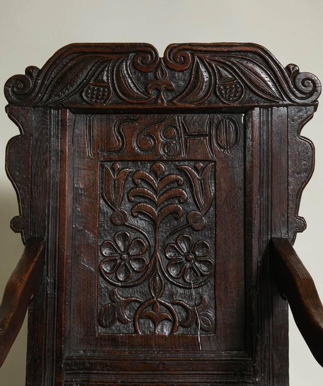 Striking 17th century English oak wainscot chair having a scrolled crest with foliage and fruit carving over a paneled back with honeysuckle vine carving and initialed 