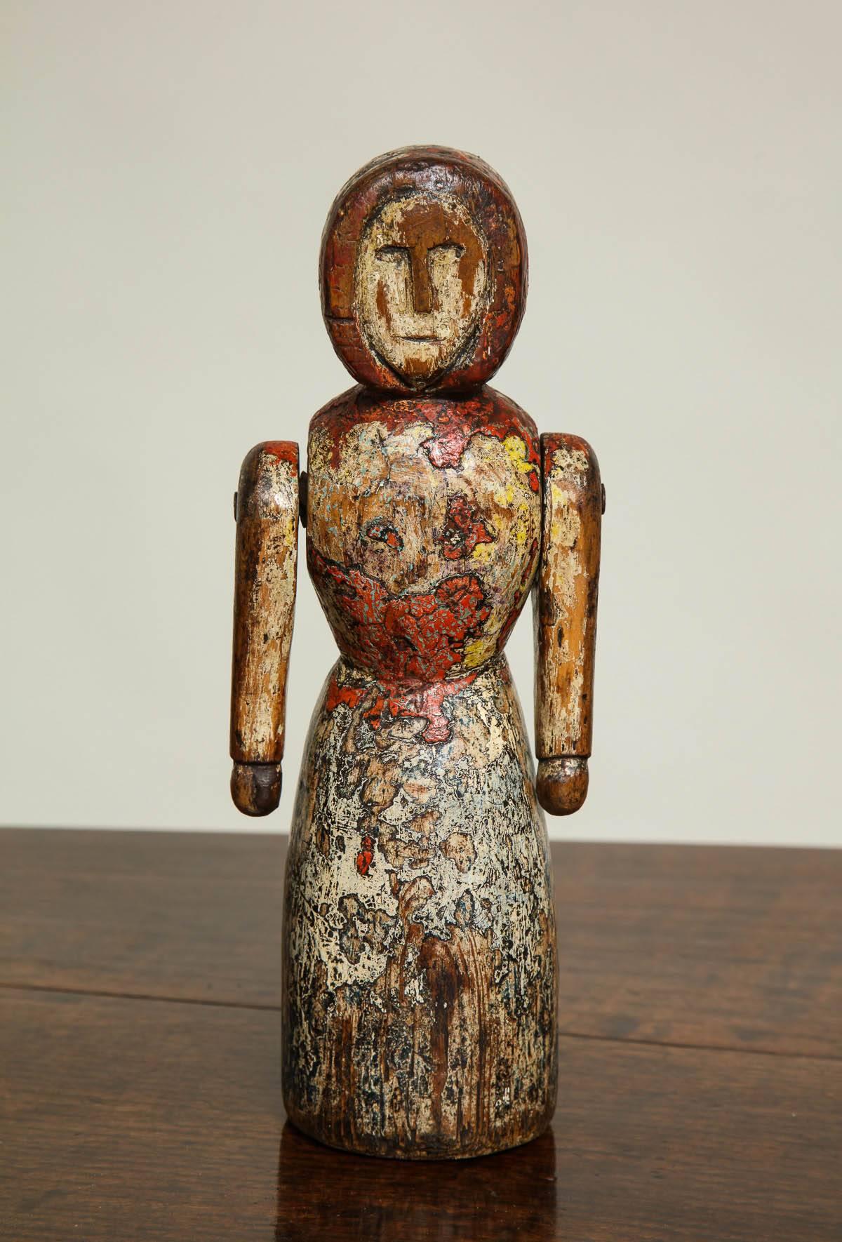 A carved wooden doll in the form of a simple bundled female figure, with moveable arms, showing traces of original paint.