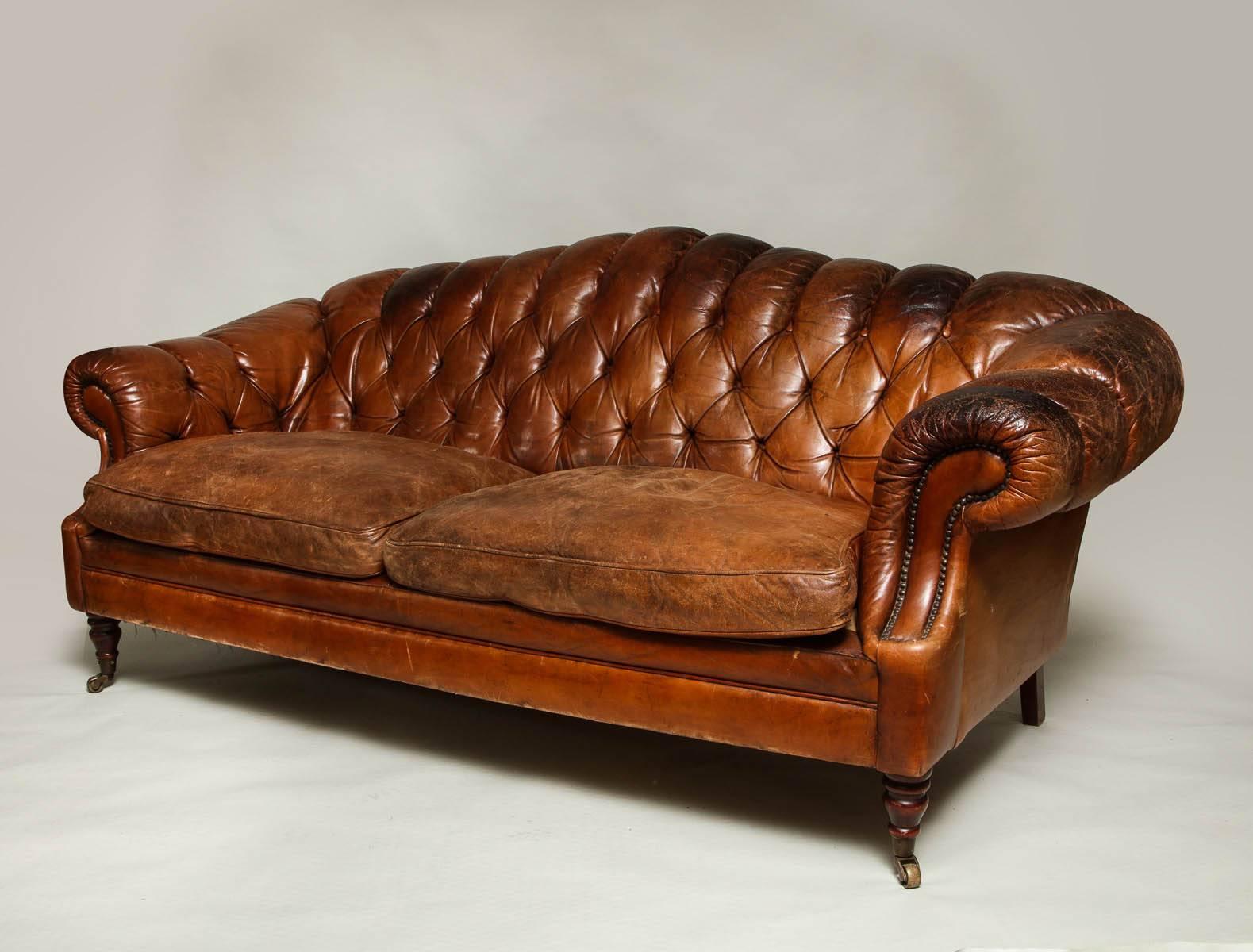 Lovely English leather sofa with rolled and tufted arms and back, two loose unbuttoned cushions, on turned legs with original brass casters, the whole with beautifully patinated tobacco leather upholstery.


 