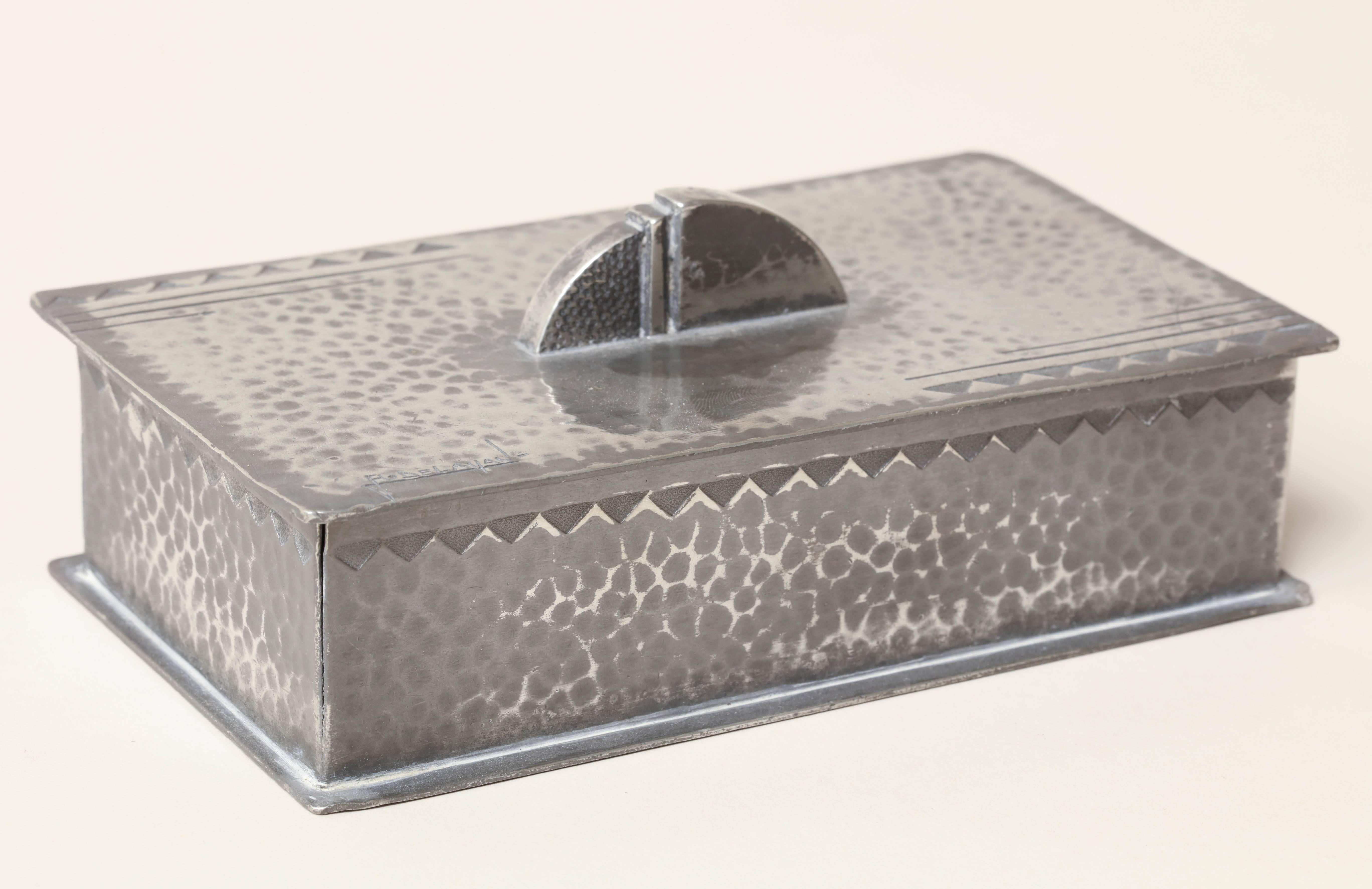 Hand-wrought rectangular dinanderie pewter martele box with triangles around rim and cubistic handle.

Signed R. Delavan on top/ impressed ETAIN GARANTI and numbered 329-2 underneath.
  