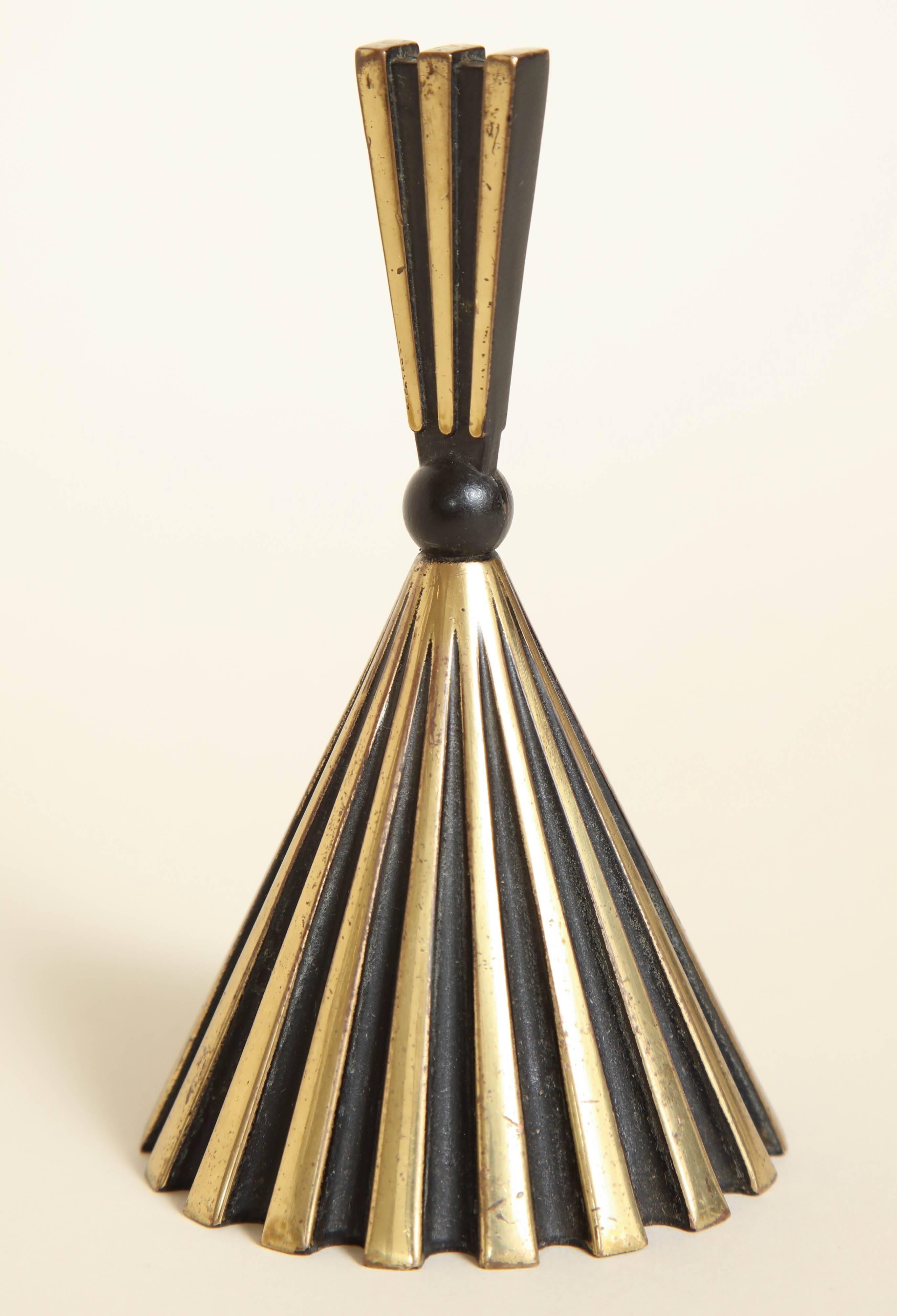 In the Bauhaus Wiener Werkstatte manner

The bell has a wide corrugated base alternating with shiny brass ribs and black matt grooves with a matching tapered grooved handle connected with a black metal bead. It is unmarked as was common. The bell is