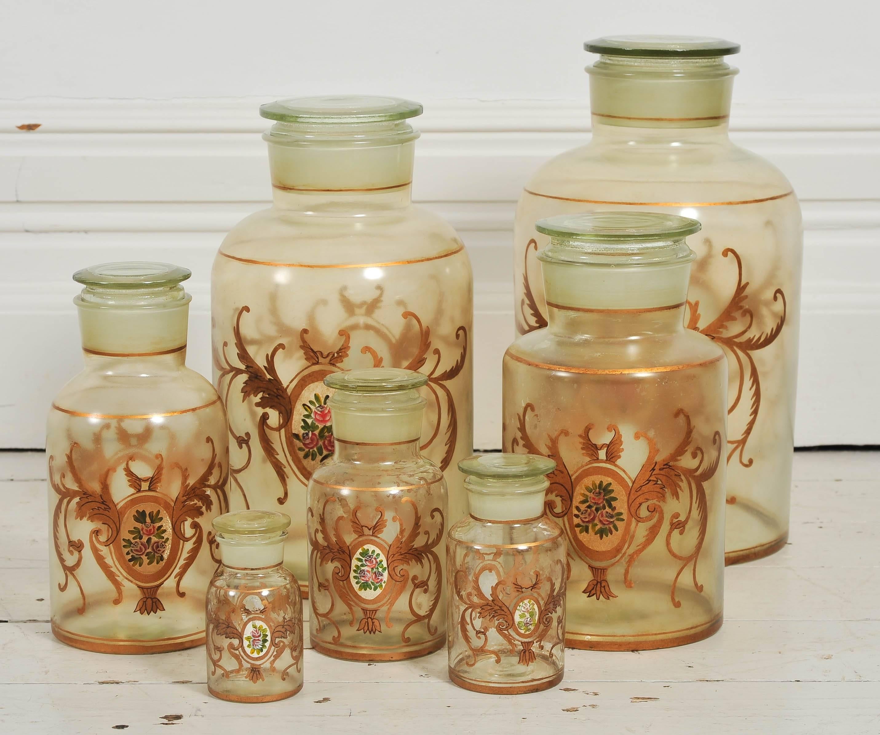 Here we have a set of seven antique apothecary jars hand decorated in gold and white. These would look wonderful in a bathroom or kitchen or on top of an armoire. 

Condition: Very good vintage condition. The small jar has a few small
