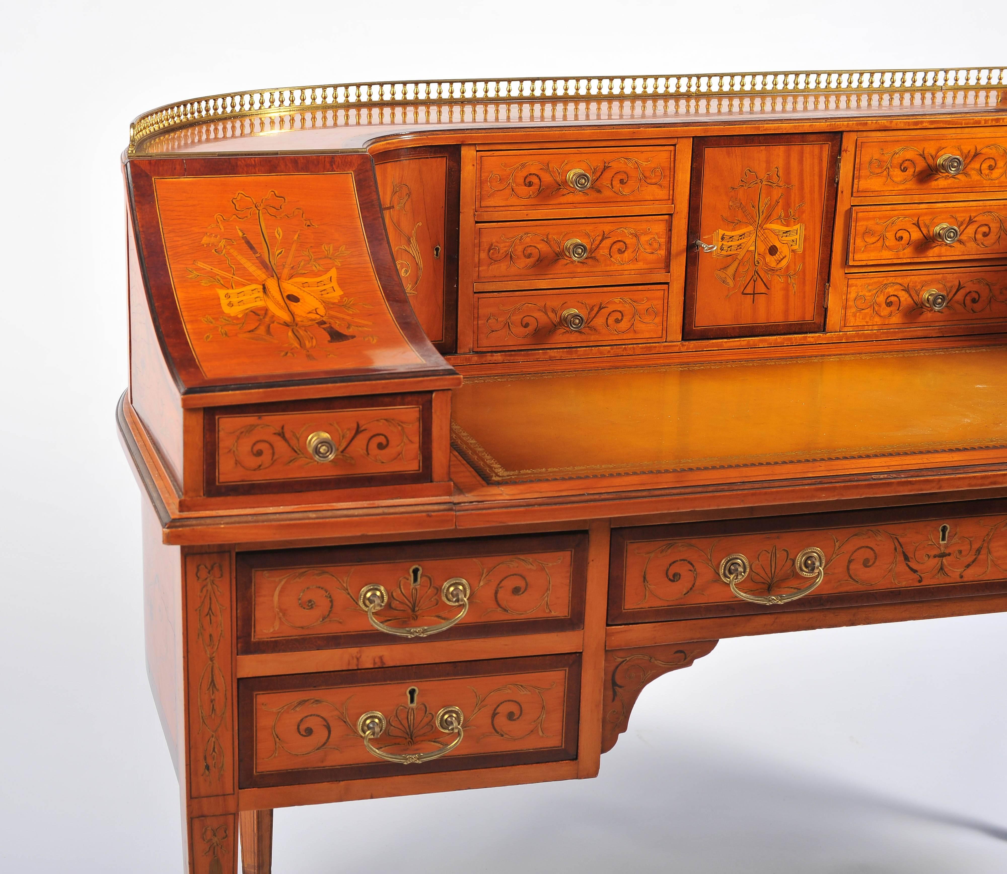 A very good quality Edwardian period Sheraton style Satinwood, Carlton house desk. Having a brass pierced gallery to the top. Marquetry inlaid decoration depicting musical instruments. Drawers and cupboards each with Rosewood crossbanding. An inset
