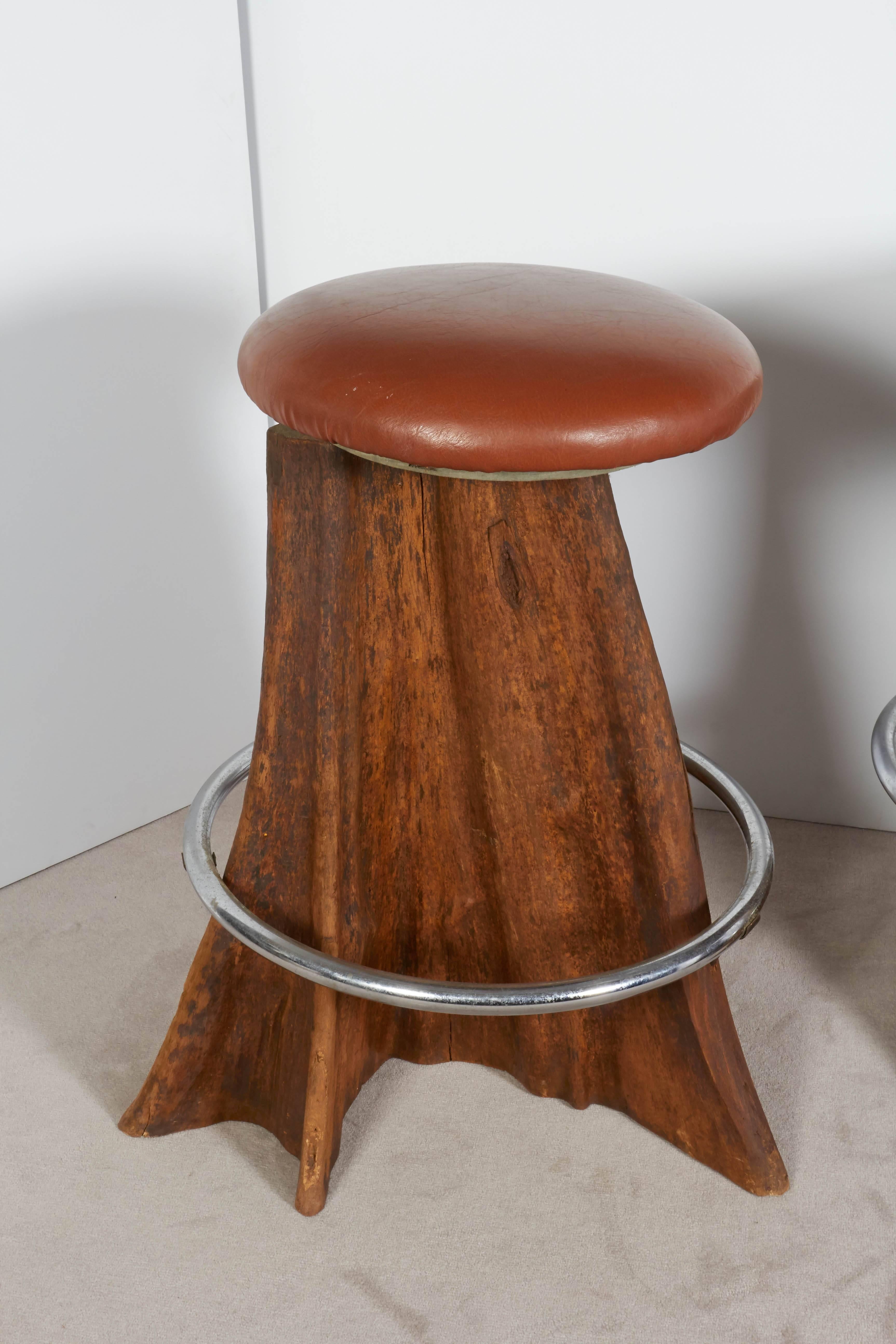 A set of three circa 1980s organic modern style swivel barstools by Brazilian designer José Zanine Caldas, each with leather seat and metal ring footrest against a cypress wood trunk as base. Excellent original condition, consistent with age and