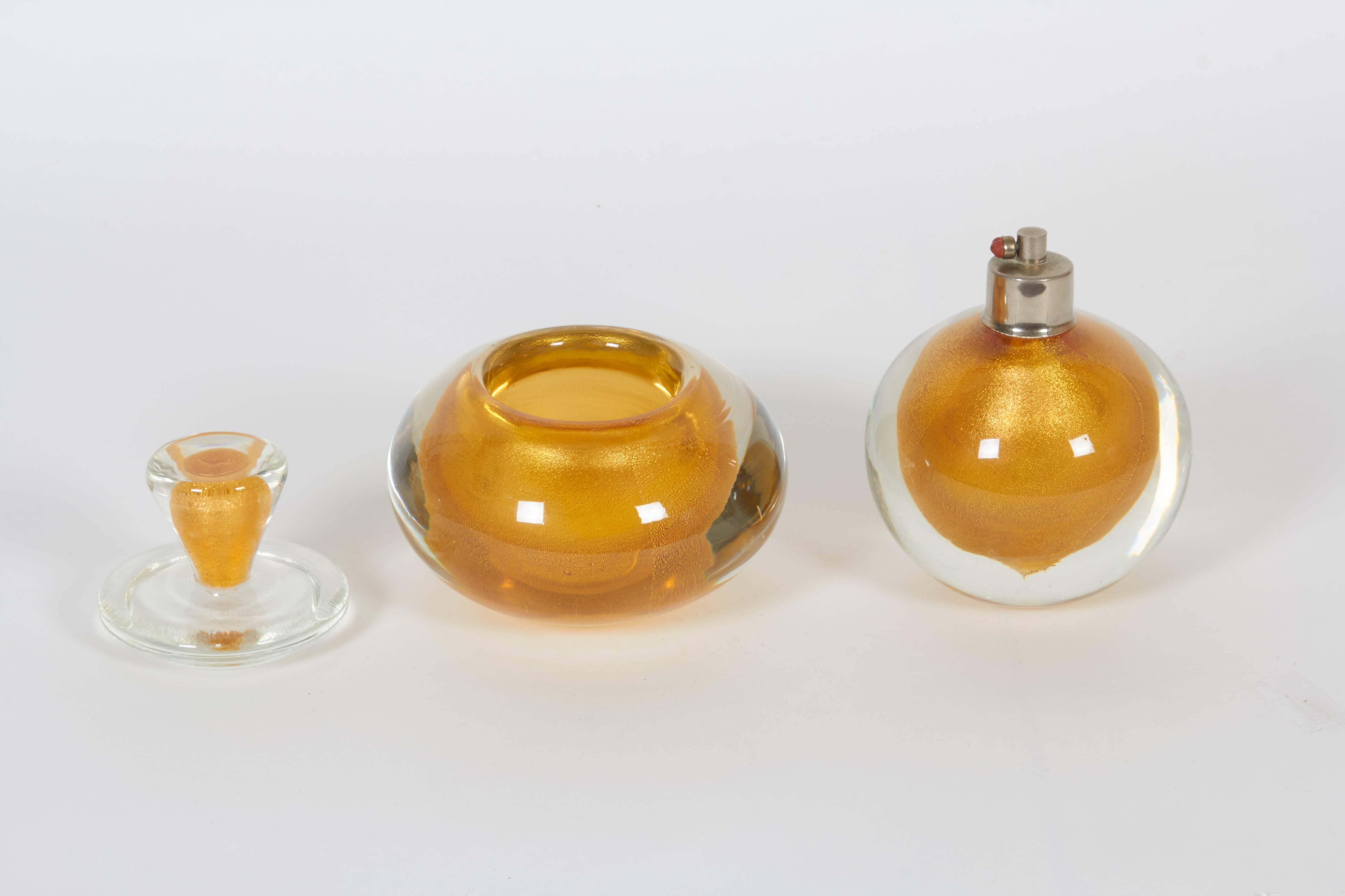A four-piece Murano glass perfume set from the Art Deco era, produced circa 1940s, comprising two perfume bottles with stoppers, a perfume bottle (with loss of atomizer) and a lidded vanity jar, each with clear Sommerso layer over iridescent gold