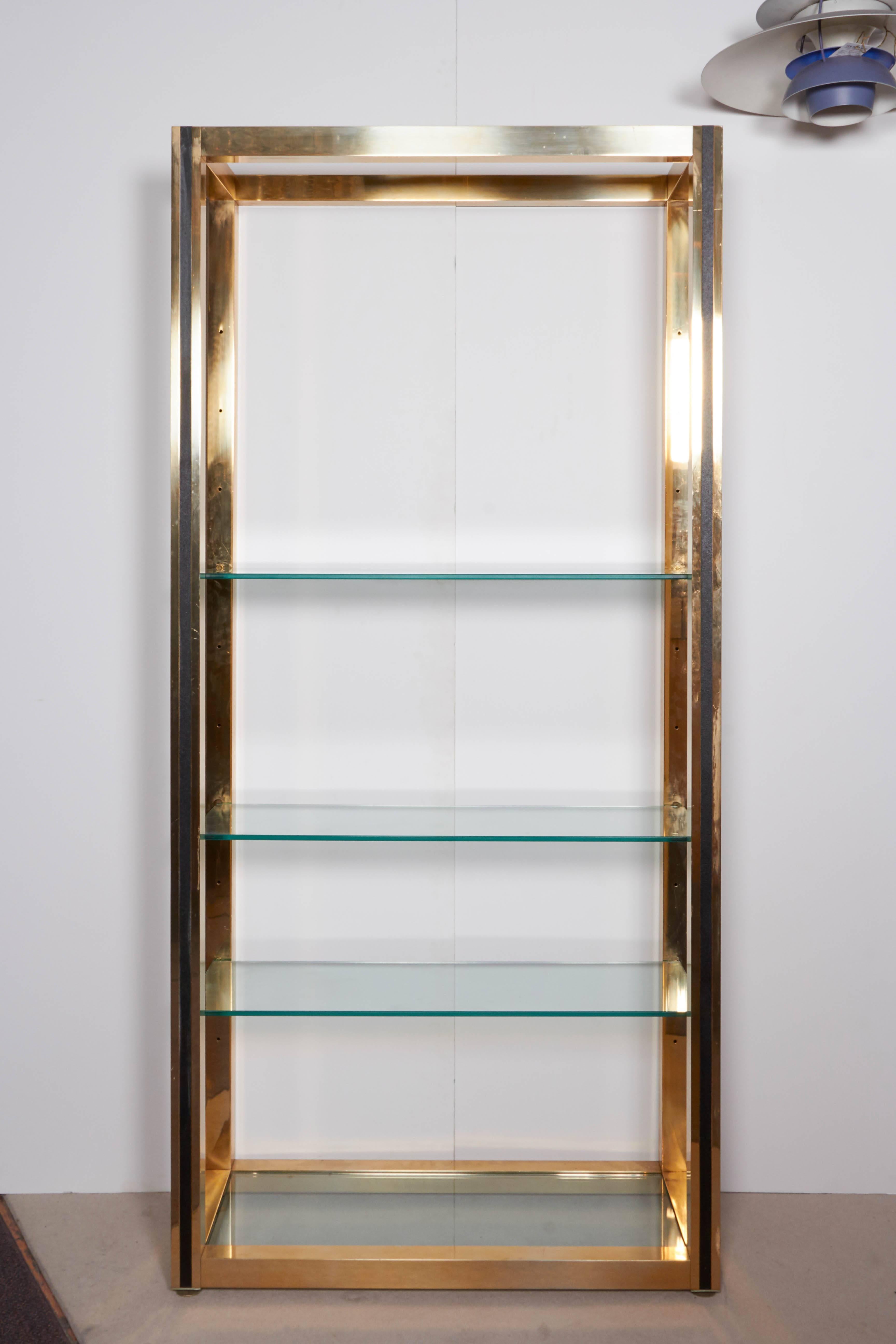 A linear Mid-Century Modern étagère produced circa 1970s and designed in the style of Milo Baughman, in brass and faux leather detailing with glass shelves. Very good vintage condition with age appropriate wear; glass requires replacement.

F34
11079