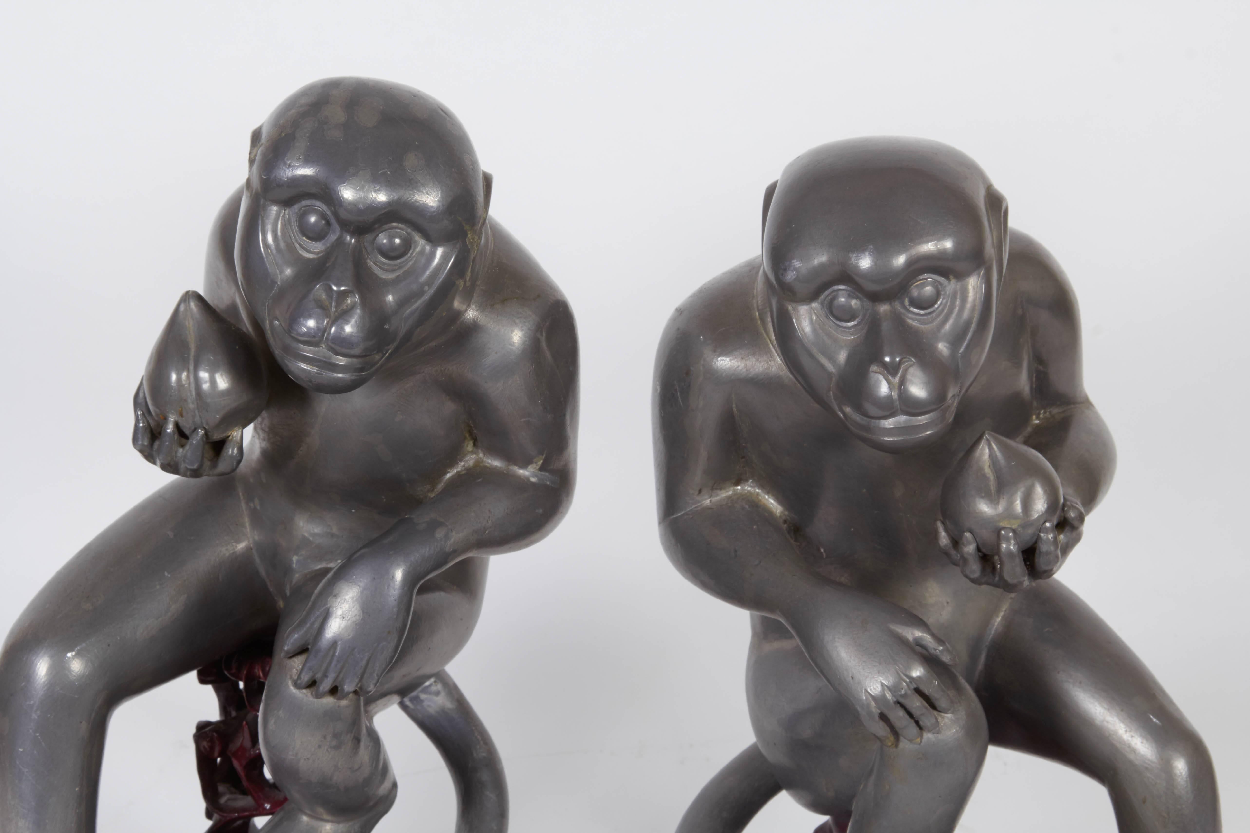 A pair of Chinese export monkey sculptures in pewter, produced circa late 19th century, obtained from the estate of Consuelo Vanderbilt, each depicted holding a peach of immortality, on carved wood stands. Very good antique condition, one monkey