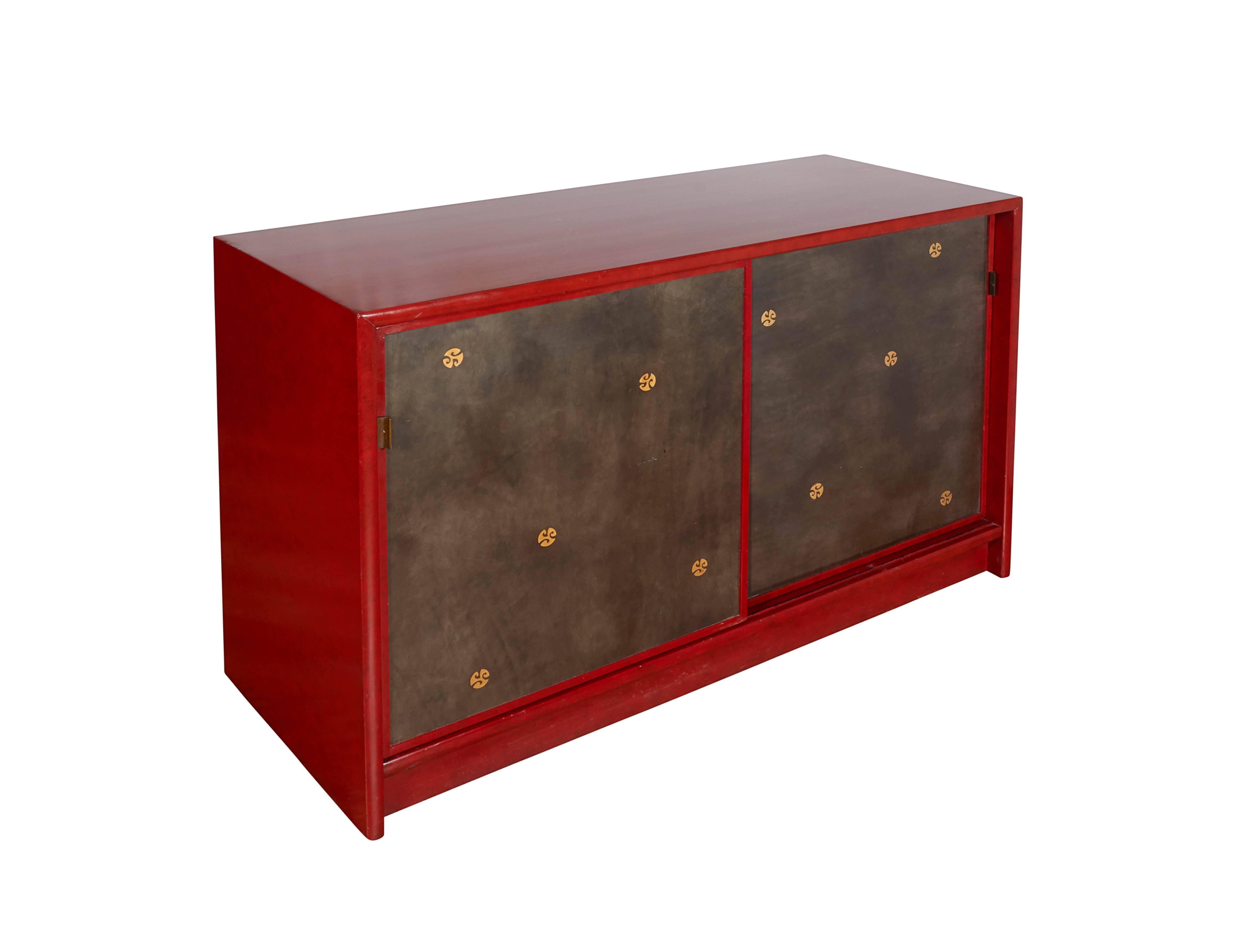 A pair of Mid-Century Modern Asian inspired cabinets or sideboards, in the style of designer Tommi Parzinger, each with red lacquer finish, including sliding doors decorated with gilt medallions, the completely gilded interiors with shelving space.