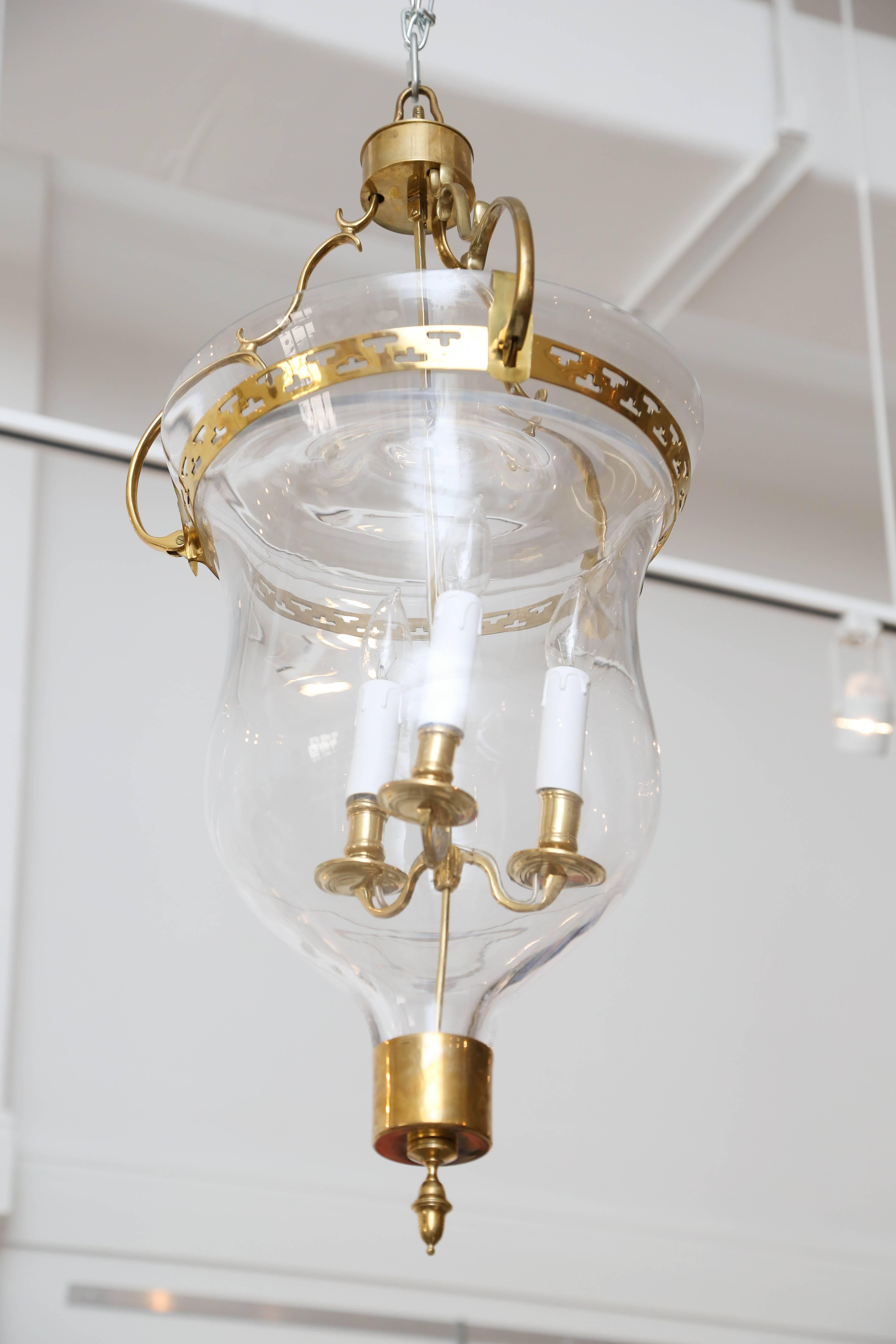 Gustavian style glass bell jar lantern with beautiful brass details
brass curved shaped arms attached to a pierced ring hold the glass bell jar, a
center stem has three arms for wired candle fixtures. Brass base and finial on the bottom. Fixture has