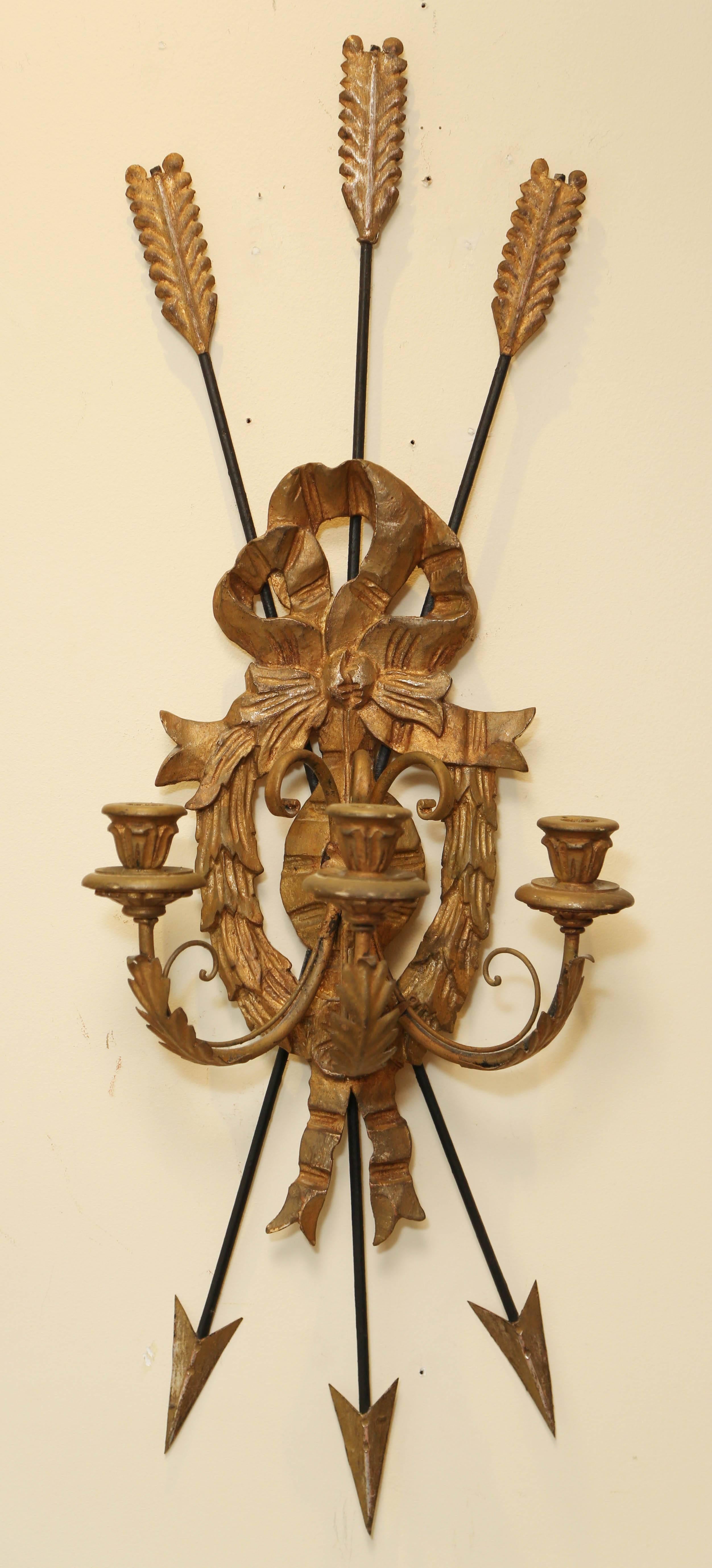 Pair of sconces, of iron and carved giltwood; each backplate having three arrows crossed behind a bow over festooning and rosette, three scrolling candlearms terminating in wooden cups. Not electrified.

Stock ID: D3487