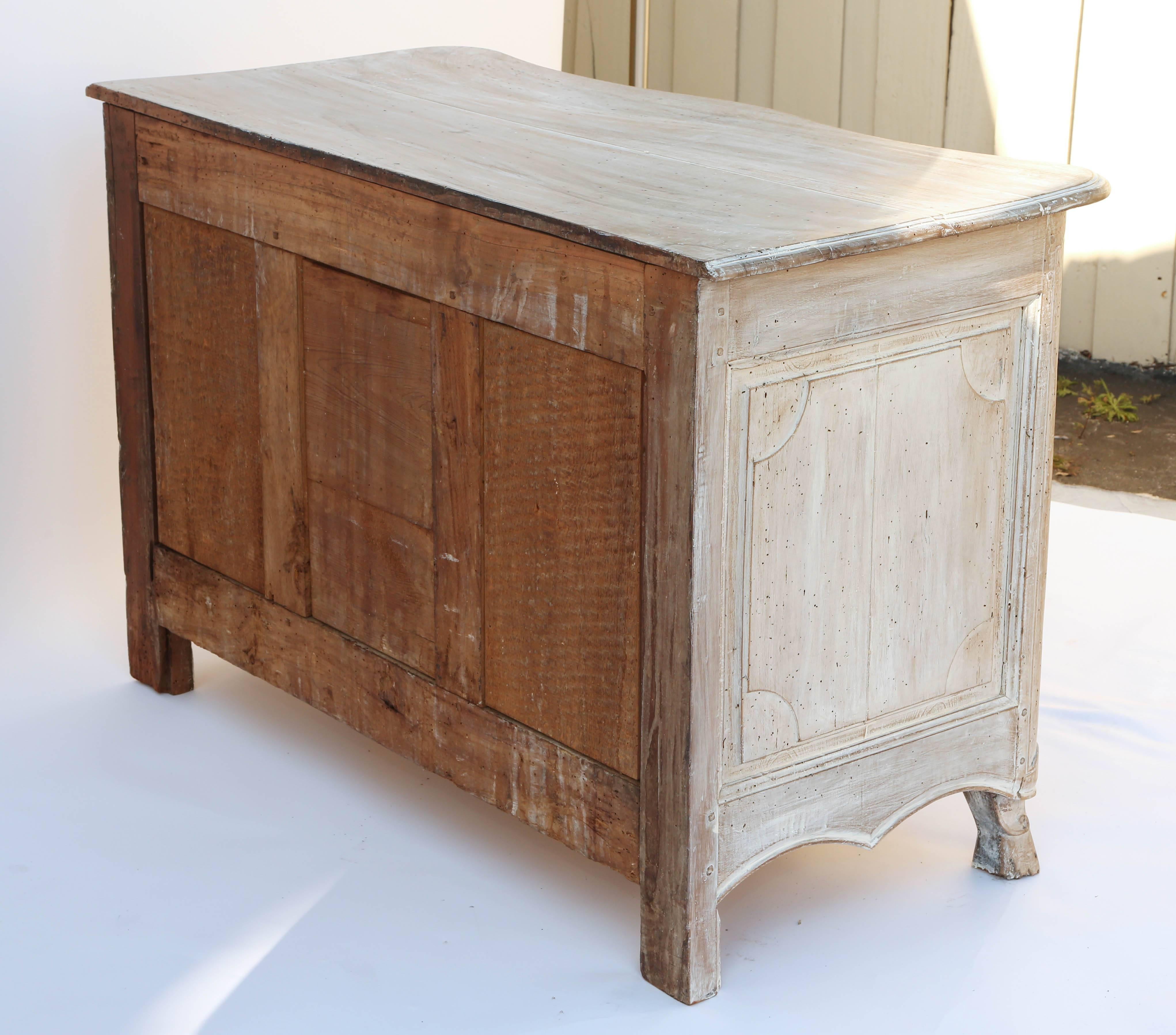 Commode, of bleached walnut with a pickled finish, having a rectangular molded top on conforming case, with rounded stiles flanking three stacked drawers, each with Rococo handles and escutcheons, inside a fielded border; with panelled sides, on