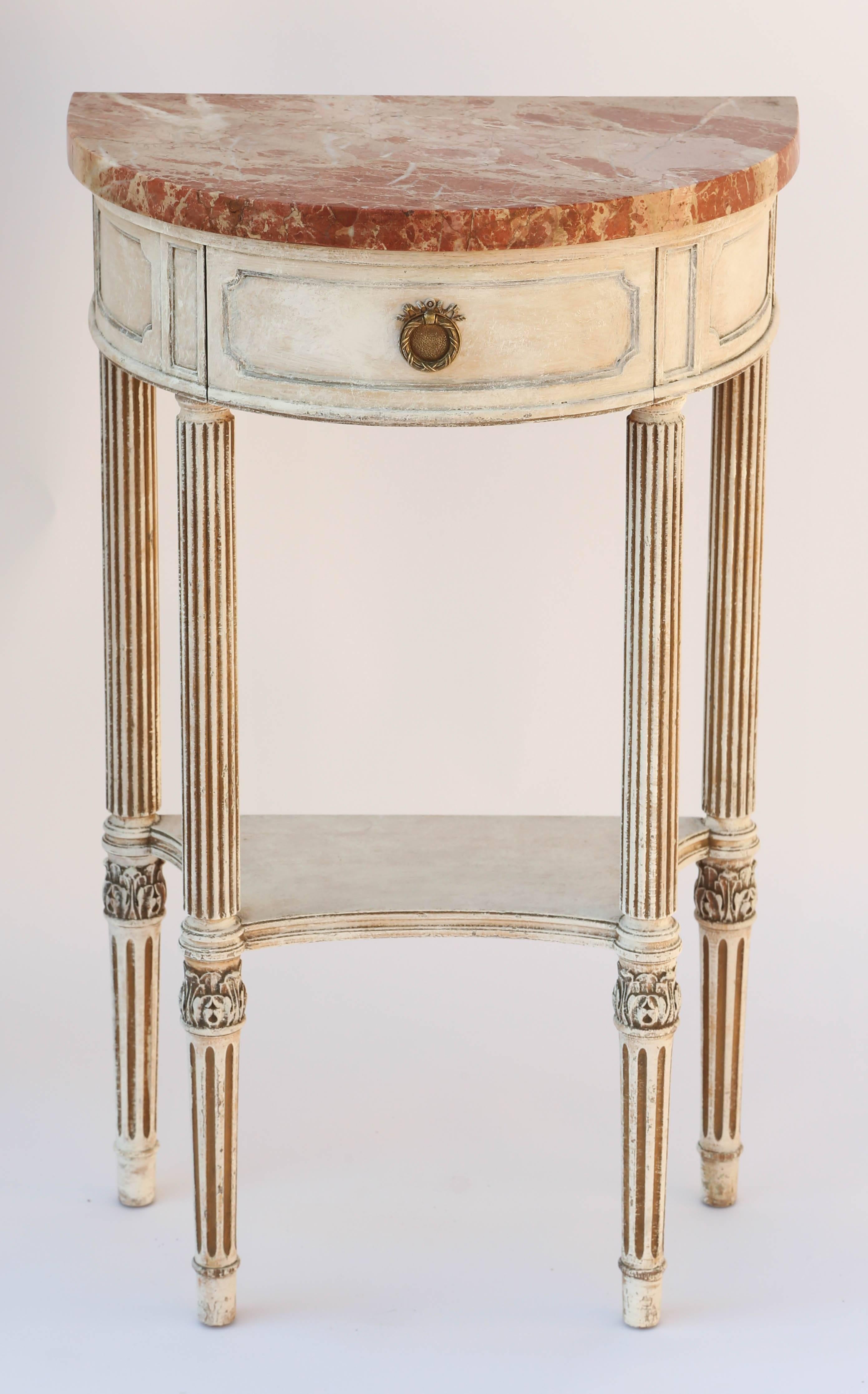 Console table, having a demilune form top of marble, on conforming table base with painted finish showing natural wear, its fielded apron with single frieze drawer, raised on round, tapering, fluted legs, joined by shelf stretcher, finished with