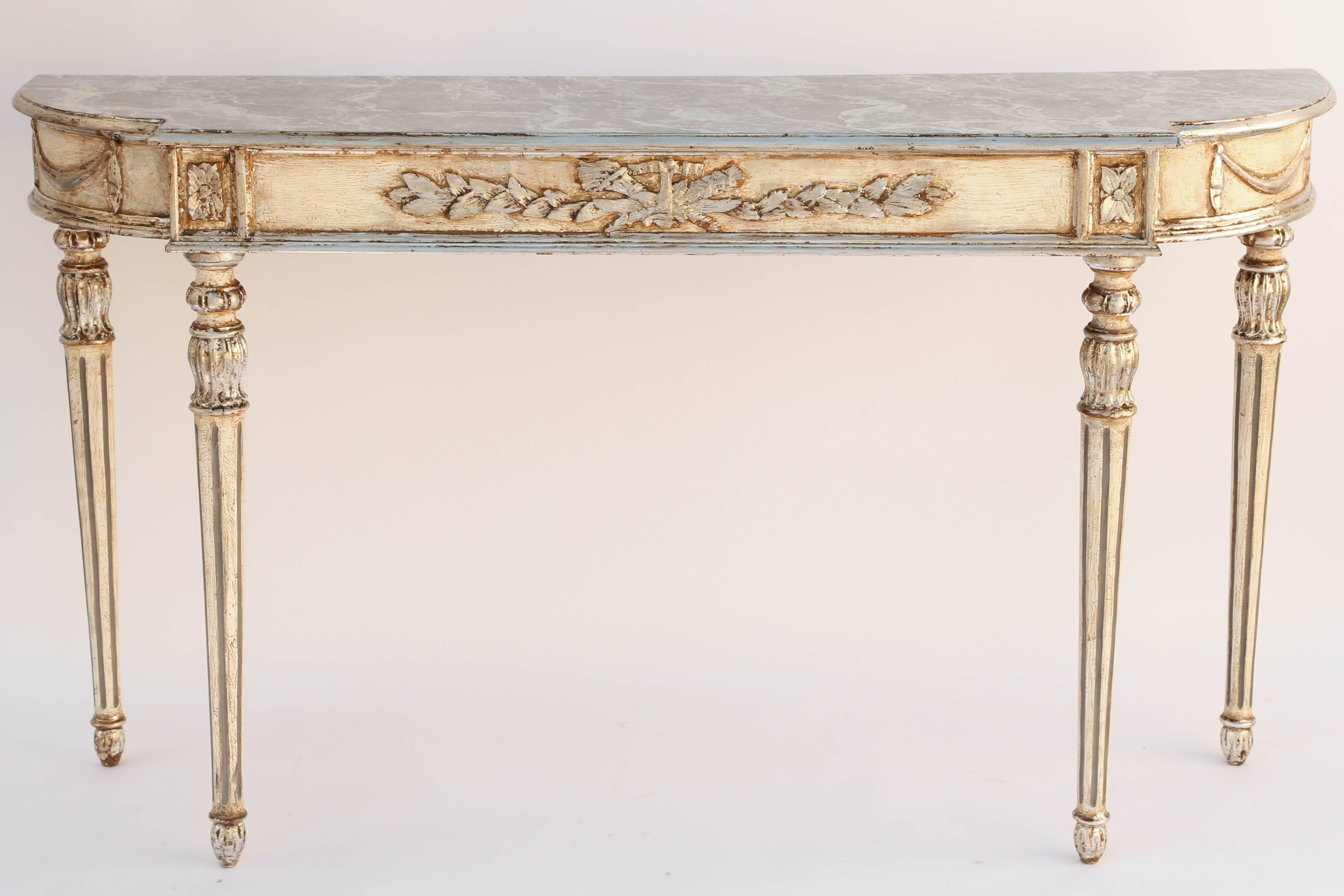 Console, having a molded, D-shaped, marbleized top, on painted and parcel silver gilt base, its fielded apron out carved with torch and quiver, flanked by laureling, with swags on each rounded corner, raised on four, fluted, tapering legs.

Stock