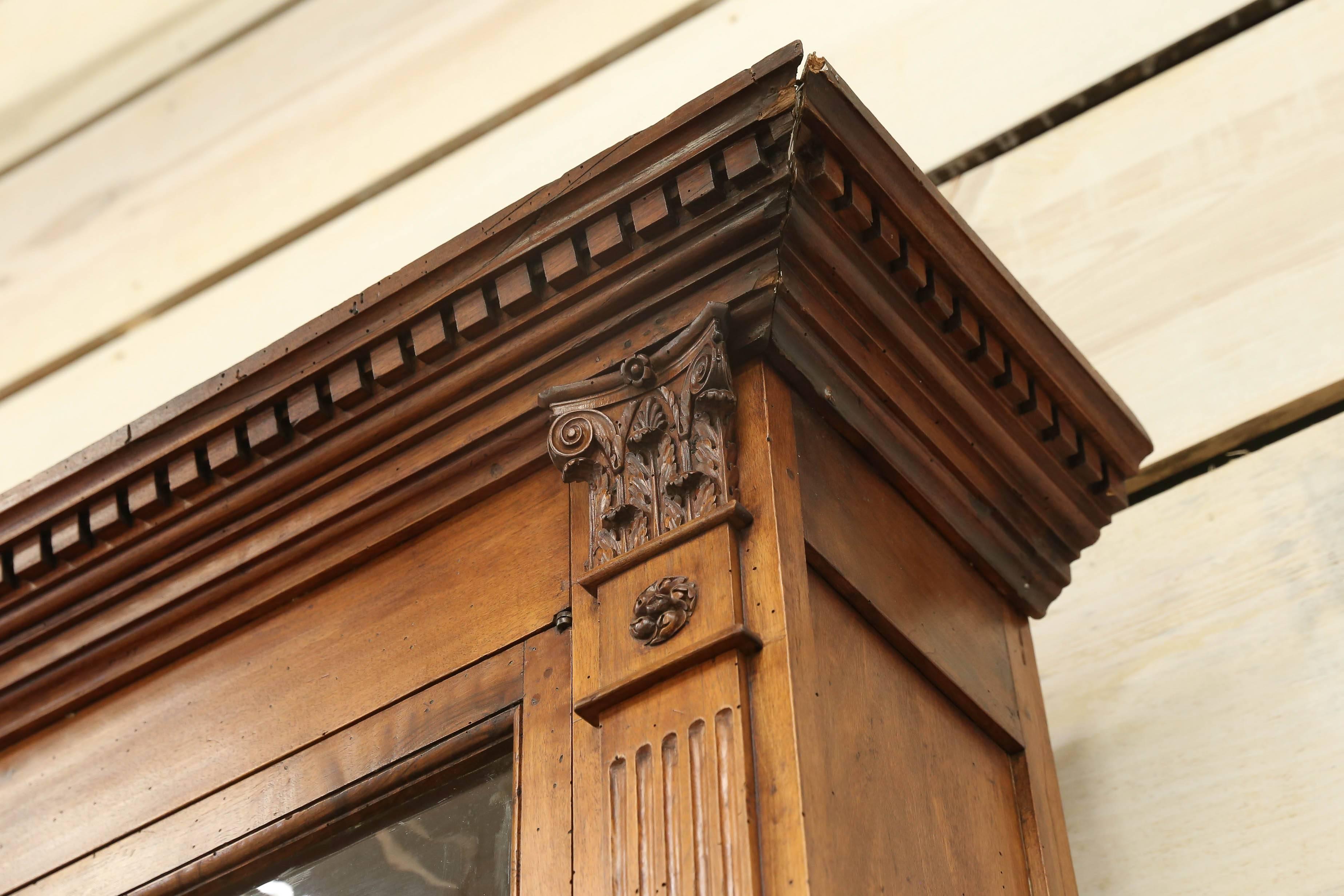 This is a two-part, handcrafted in walnut, Italian cabinet that was used in either a pharmacy or as a bookcase. It still has it's original handblown glass doors and the shelves are adjustable. The handsome carving with columns, capitals and dentil