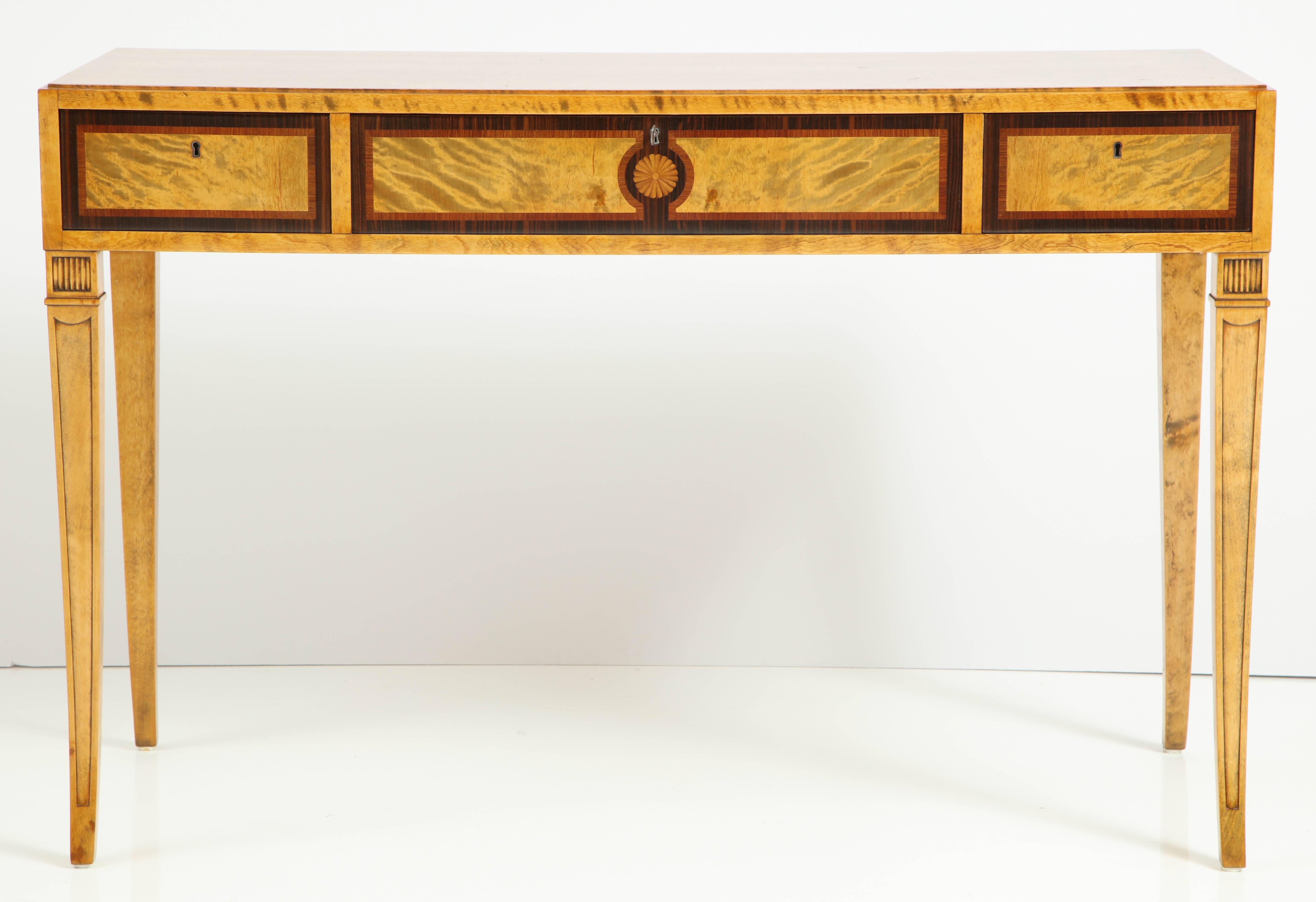 A Swedish Grace birch, fruitwood and rosewood inlaid console, circa 1940s, the rectangular steeped top with and inlaid frieze and three drawers raised on square out curved tapered and channeled legs.

Could also be used as a small writing table.