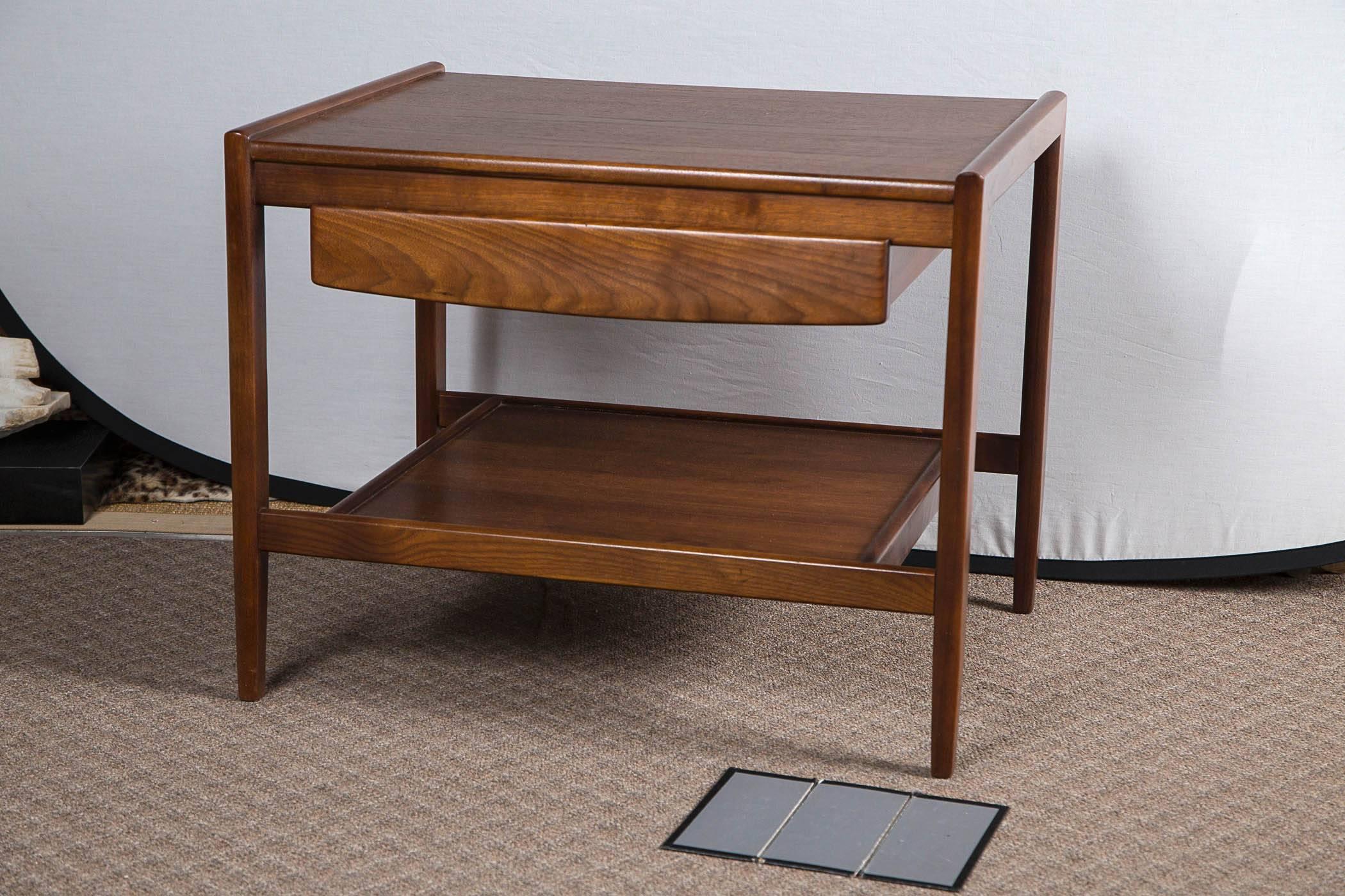 Pair of quality walnut side tables with drawer and lower shelf by John Stuart. Beautiful patina to walnut with original finish in excellent condition. Back of table is finished and duplicates detail on front.