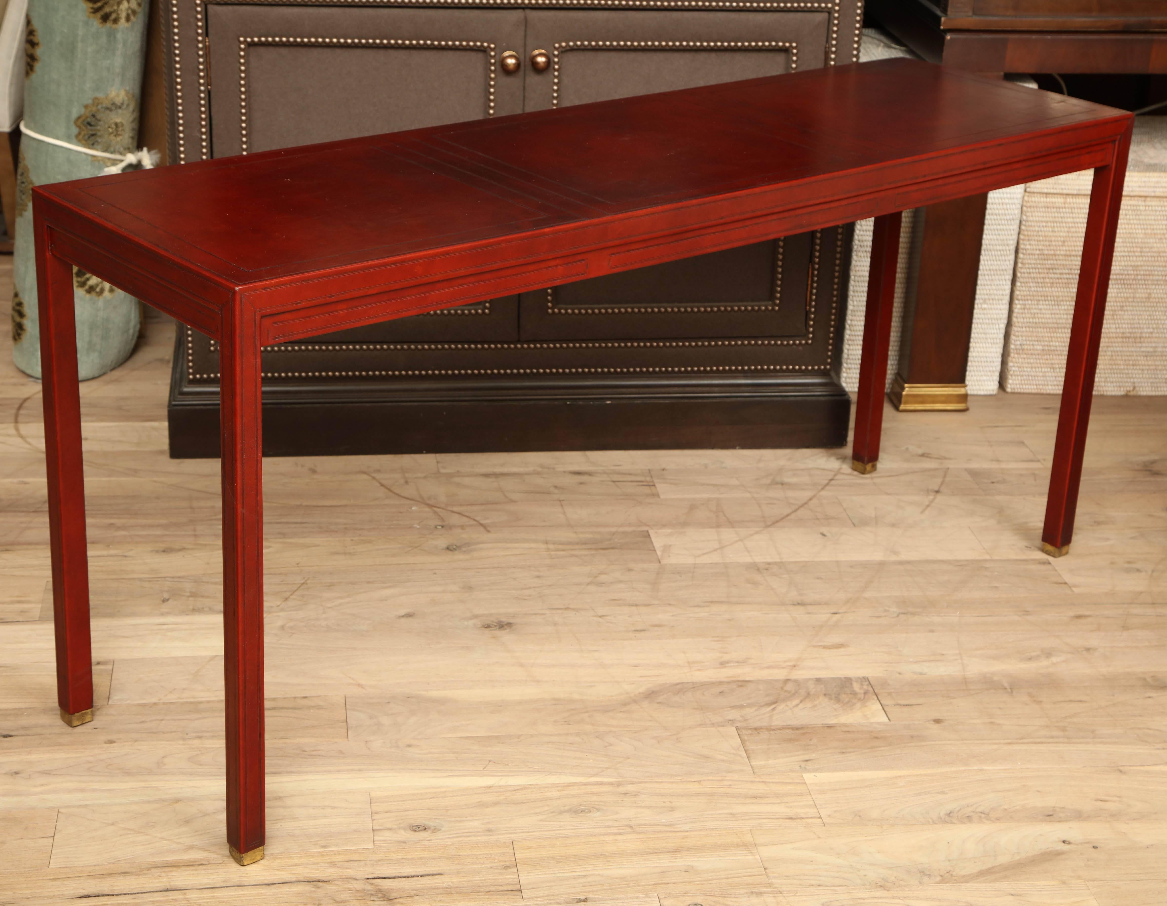 Walnut console table with brass feet, circa 1970, restored and clad in russet leather with blind tooled surface.