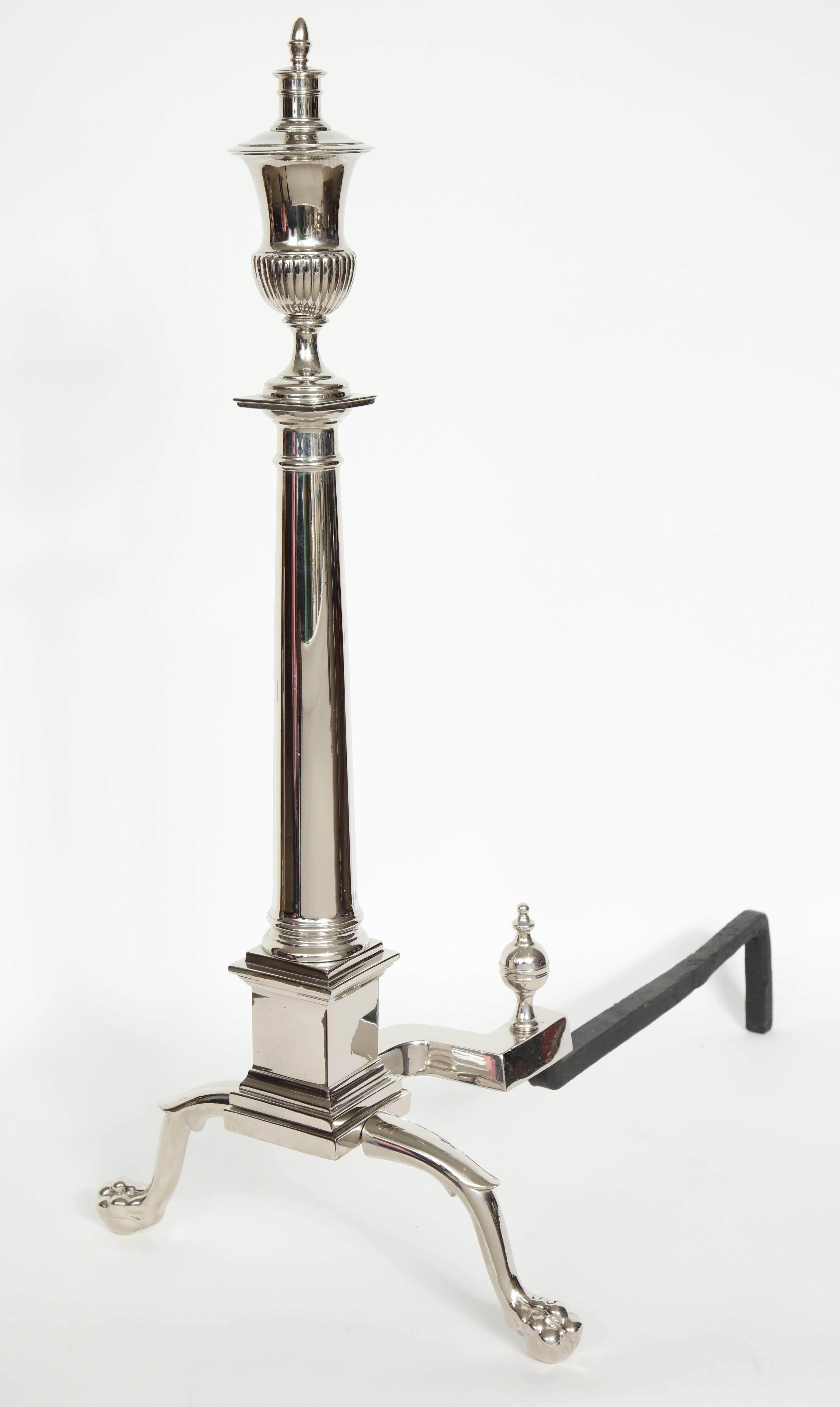 Pair of large-scale polished nickel andirons with a tapering column and a fluted urn finial resting on stylized paw feet.